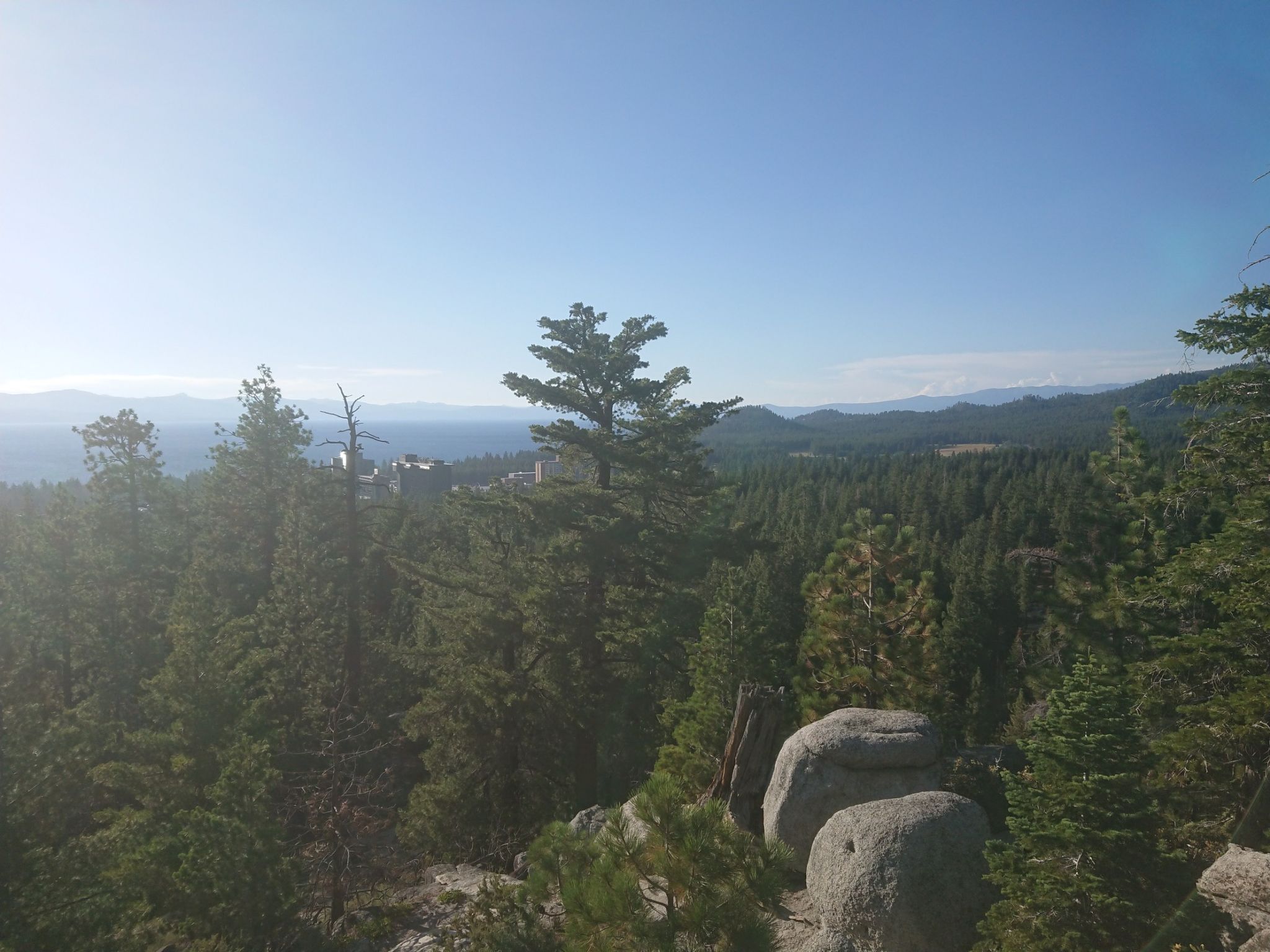 Sunny view through tall pines over a vast forest and distant hazy landscape. - Van Sickle Trailhead – Lake Tahoe Vista Point loop from Van Sickle Bi-State Park