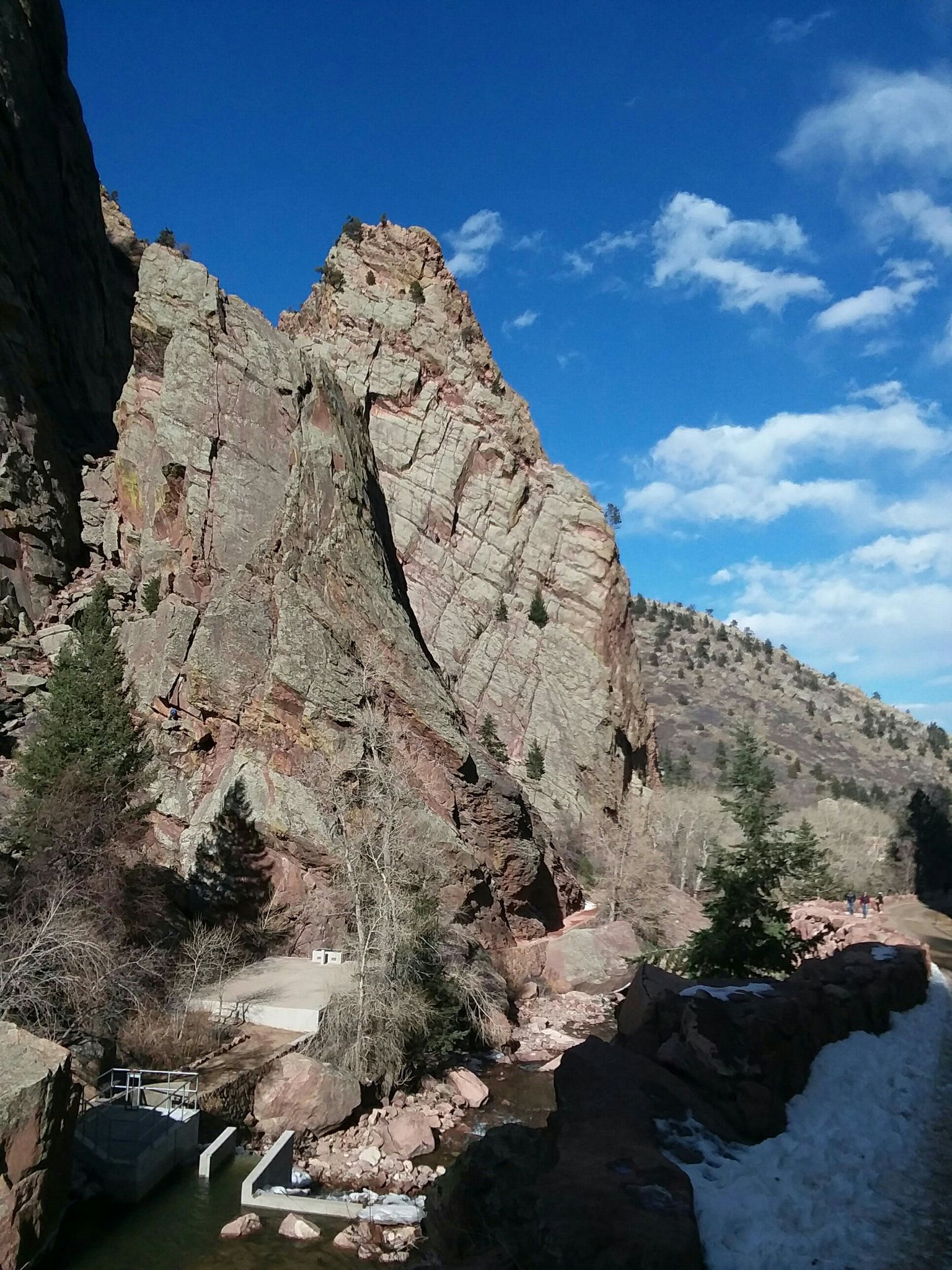Towering red rock cliff beside a river, with blue sky and clouds. - View of the Mountain Landscape – View of Eldorado Canyon loop from Eldorado Springs Pool