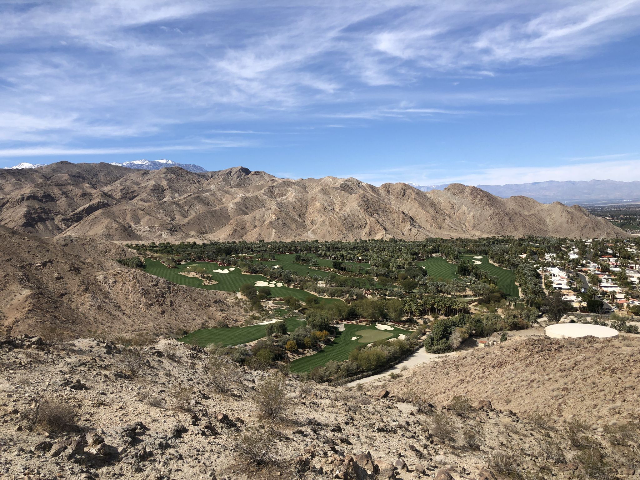 Panoramic view of a green golf course nestled among barren mountains under a bright sky. - Hopalong Cassidy Loop