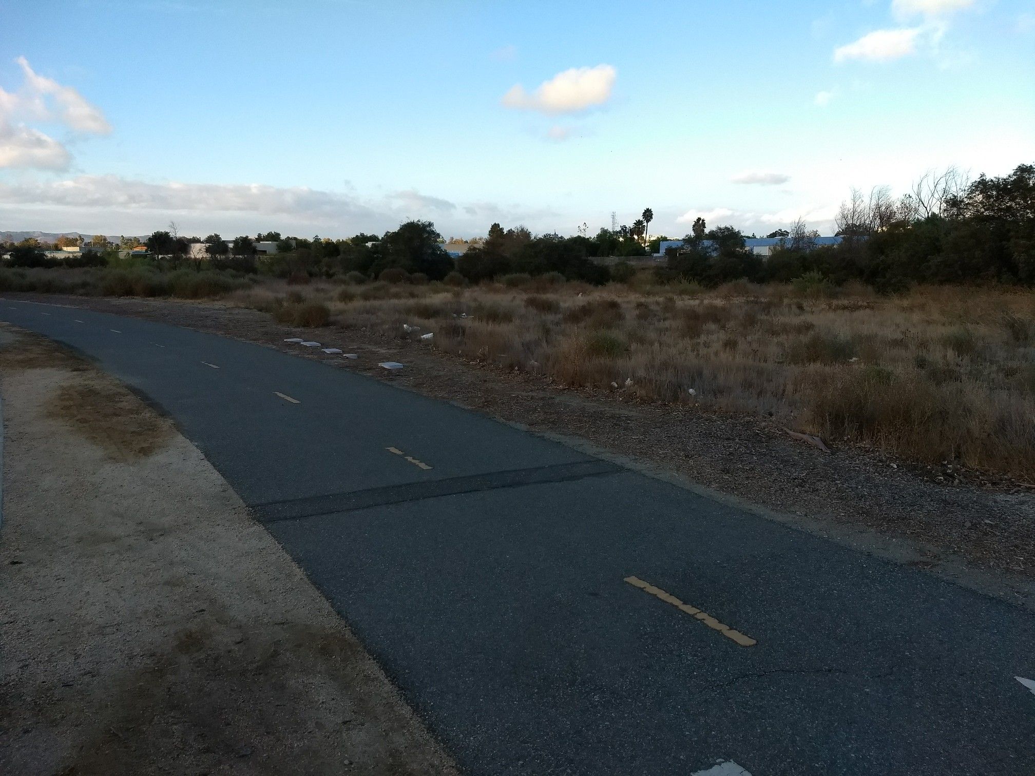 Paved road with yellow lines next to dry fields under a cloudy sky. - City of Temecula Civic Center – Old Town Temecula loop from Ortega Oaks Plaza