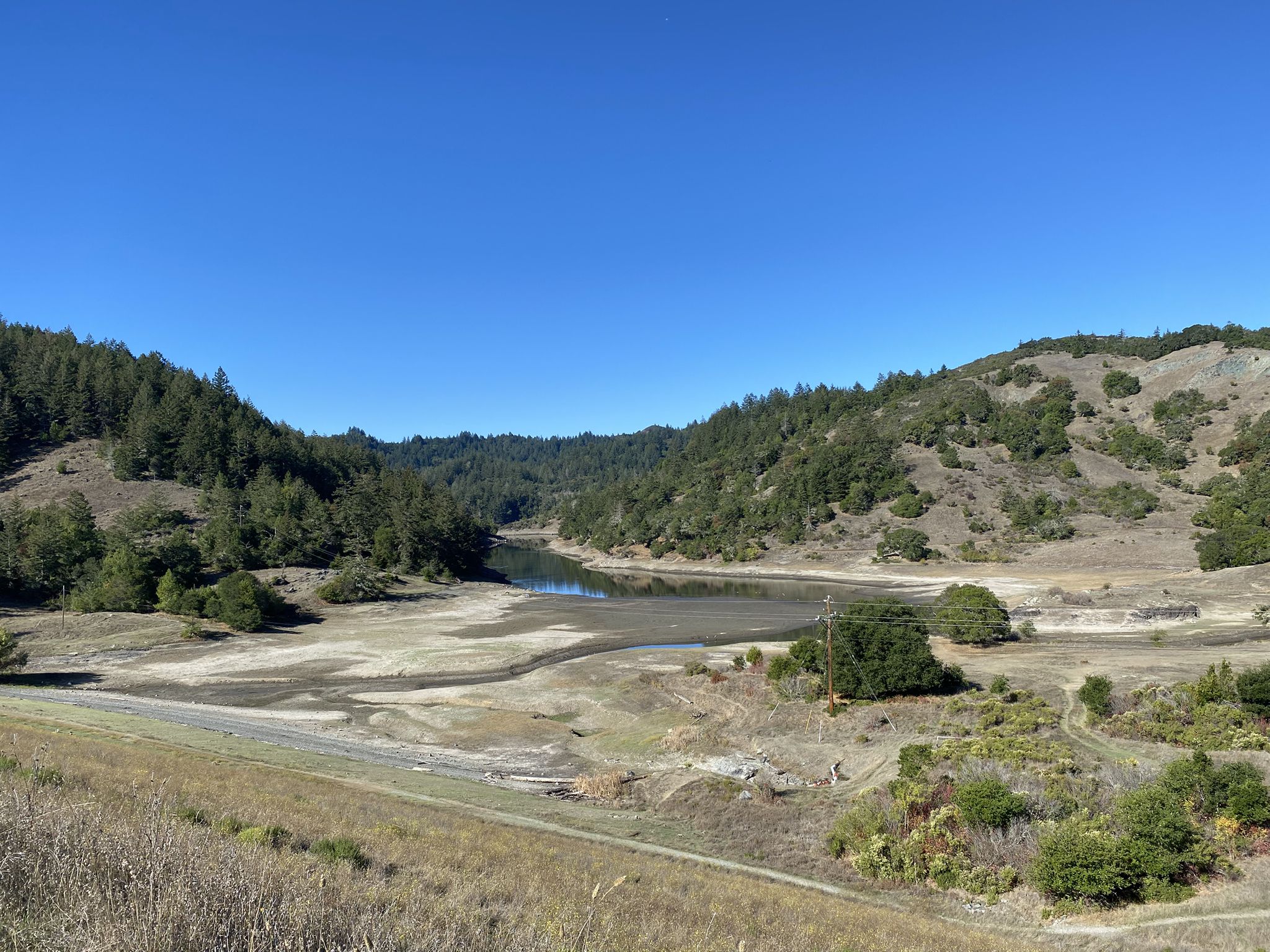 Partially dry lakebed surrounded by hills with sparse trees on a clear day. - Bon Tempe Lake and Cataract Falls Loop Trail