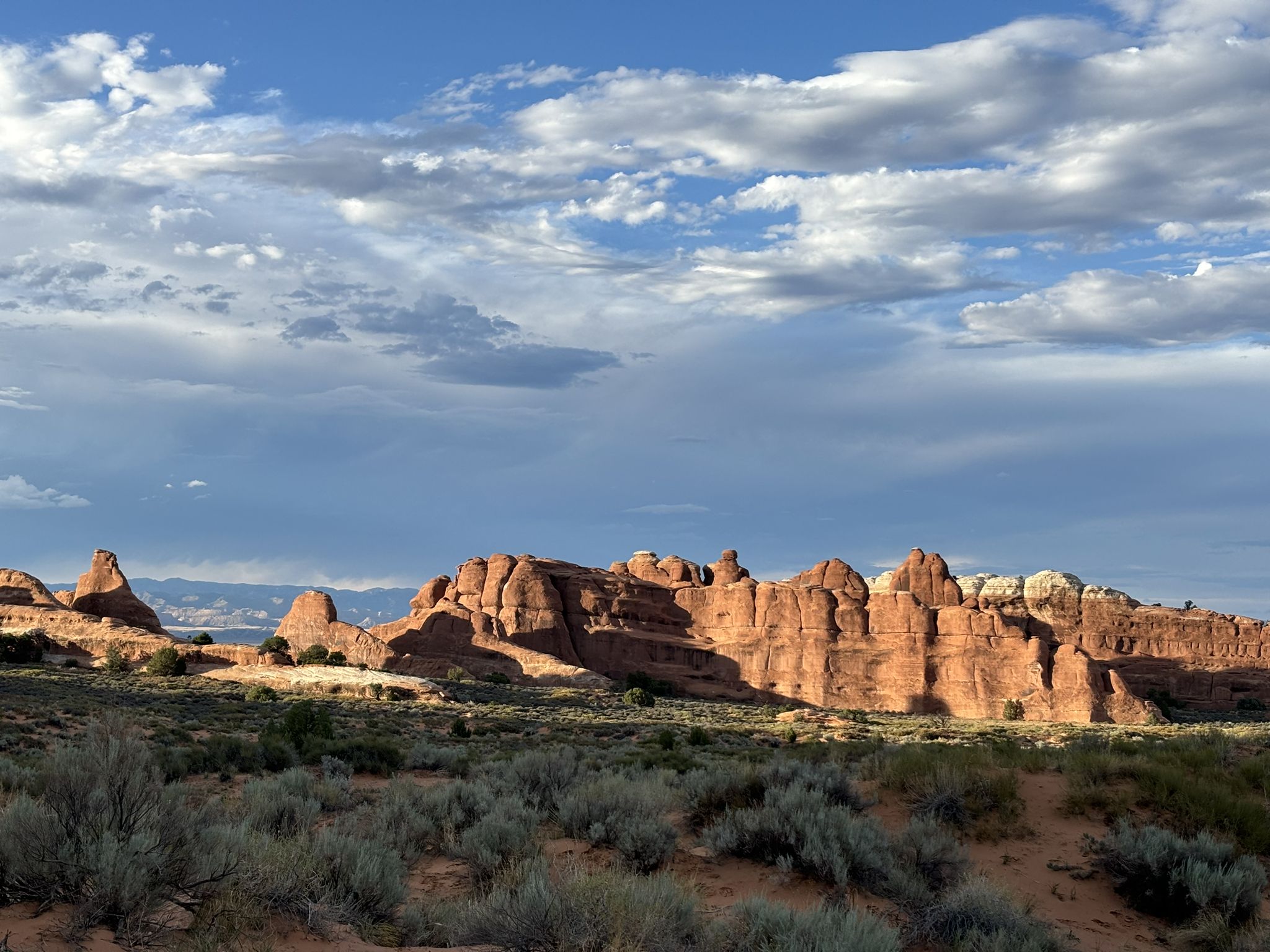 Distant red rock formations lit by sunlight under a dramatic cloudy sky. - Landscape Arch Trail