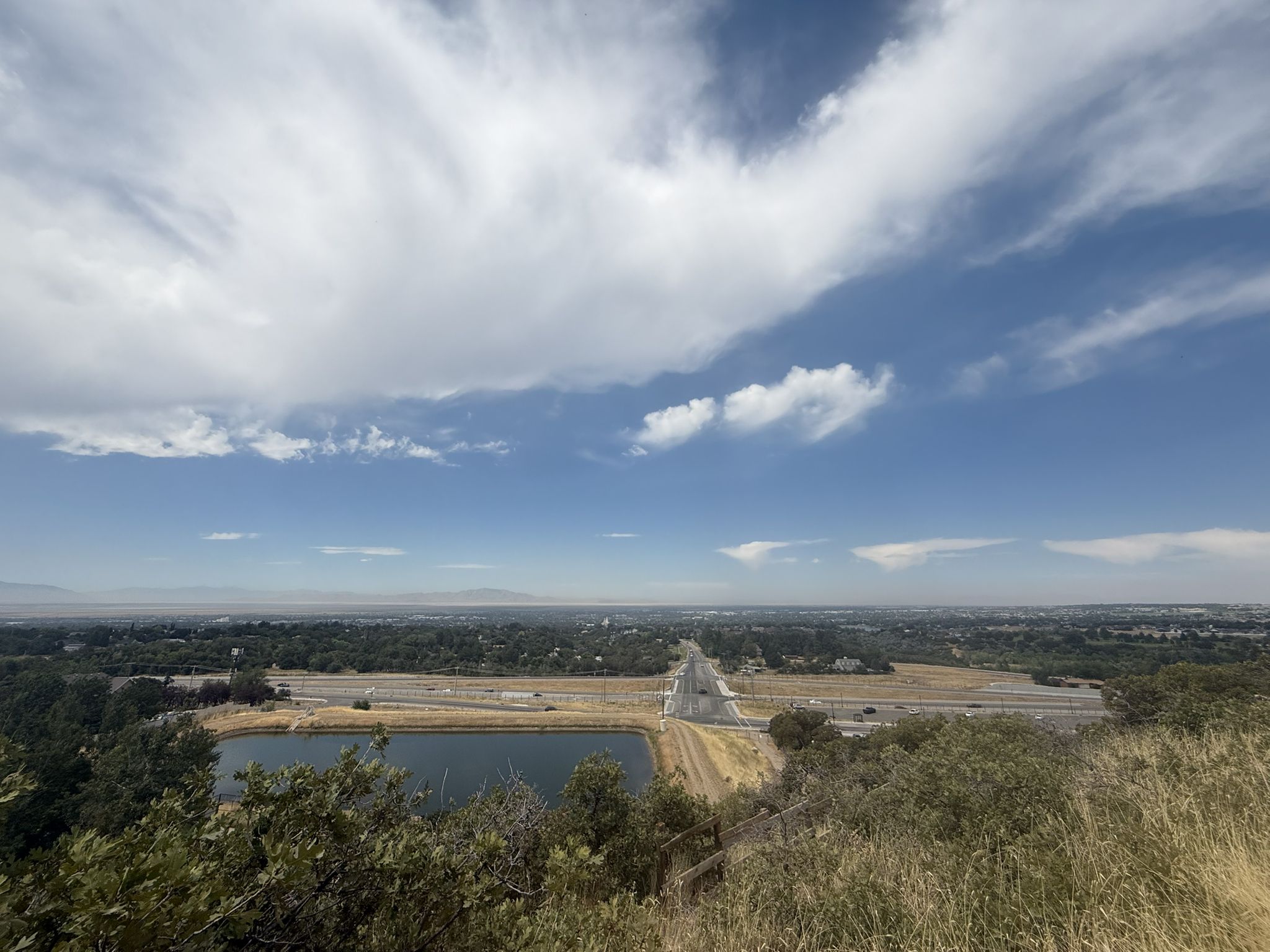 Overlook of a lake, highway, and distant city under a cloudy sky. - Adam’s Canyon Lower Falls