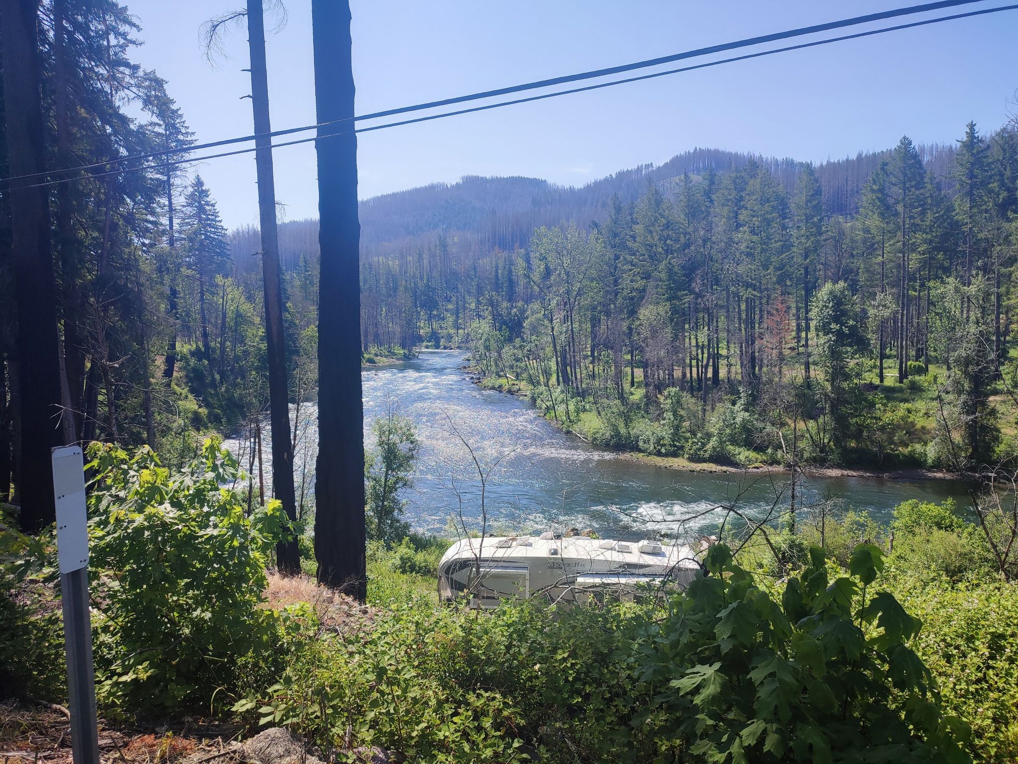 A river flows through a forested valley with an RV parked nearby. - Blue River Reservoir via TransAmerica Trail
