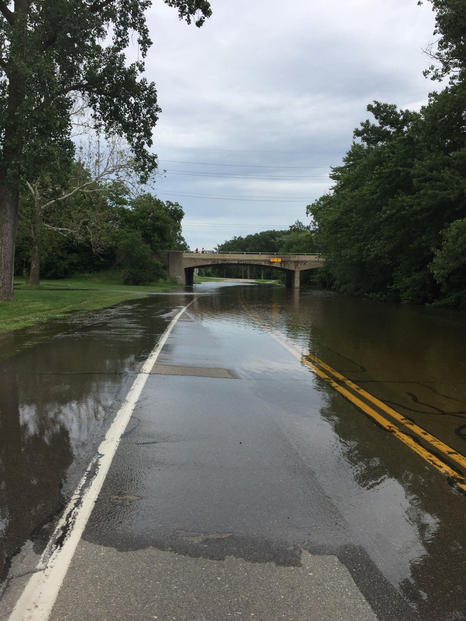 A flooded paved road leads to a bridge under an overcast sky. - Middle River Rouge loop from Dearborn Heights