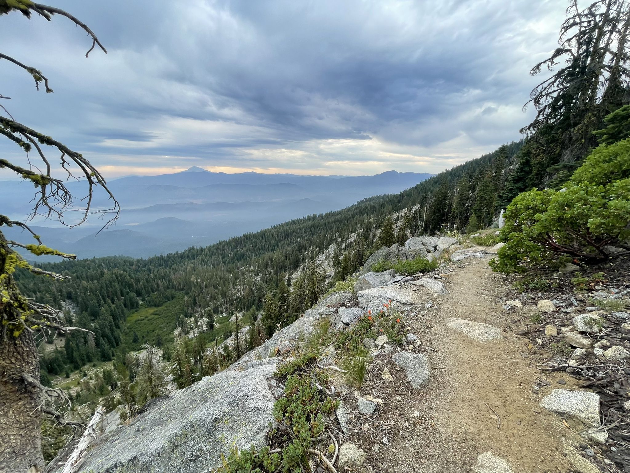 Dirt trail on a mountain slope overlooking a hazy forested valley. - Paynes Lake via Pacific Crest Trail
