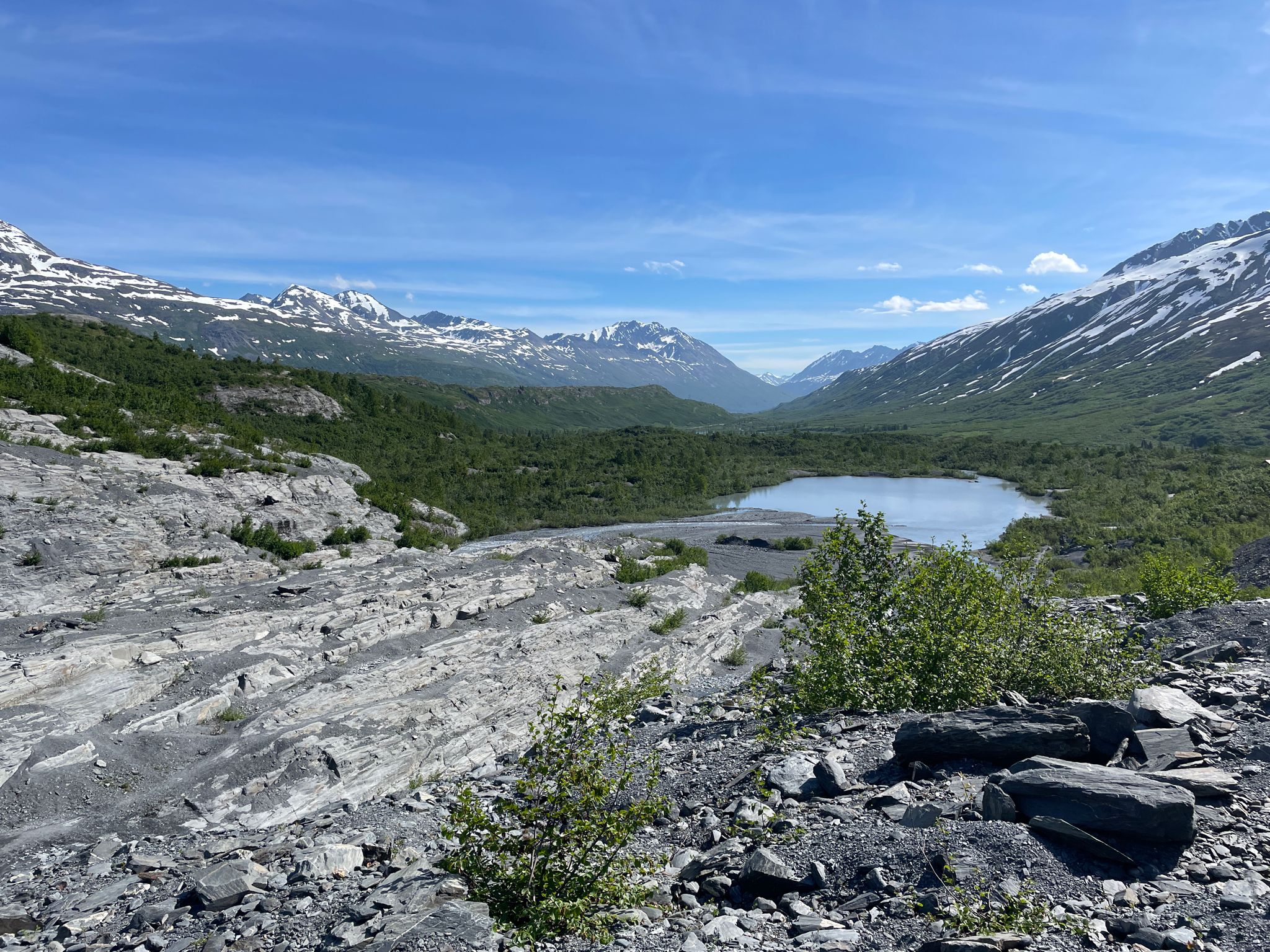 Sunny glacial valley with a clear lake, rocky foreground, and snow-capped mountains. - Worthington Glacier Ridge Trail