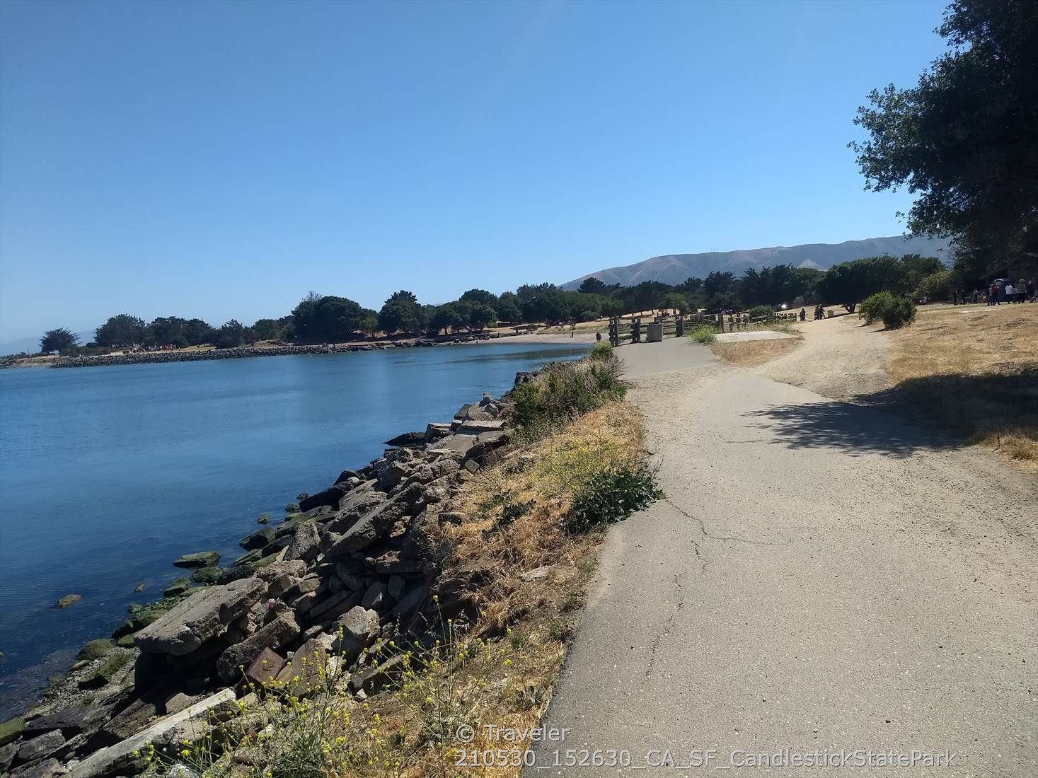 Paved path alongside a rocky shore and calm blue water. - Candlestick Point