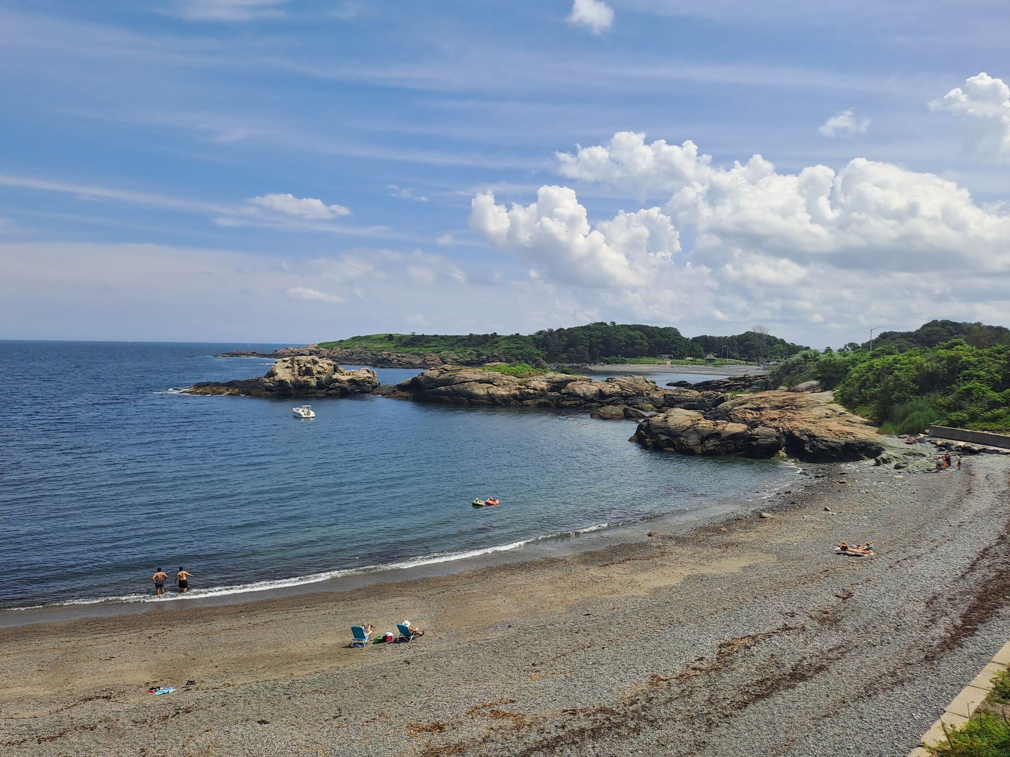 Sunny beach with people relaxing, calm blue water, and rocky coastline. - Views from Nahant Road – Forty Steps Beach loop from Revere Beach