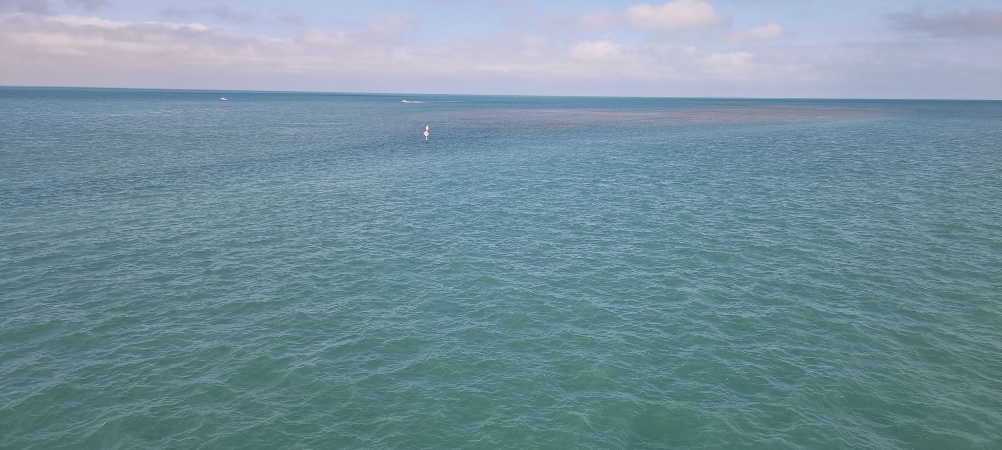 Calm blue-green ocean under a partly cloudy sky with a distant white object. - Old 7 Mile Bridge