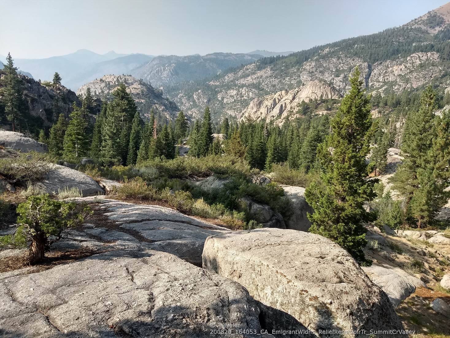 Rocky landscape with pine trees and distant mountains under a bright sky. - Relief Reservoir Trail