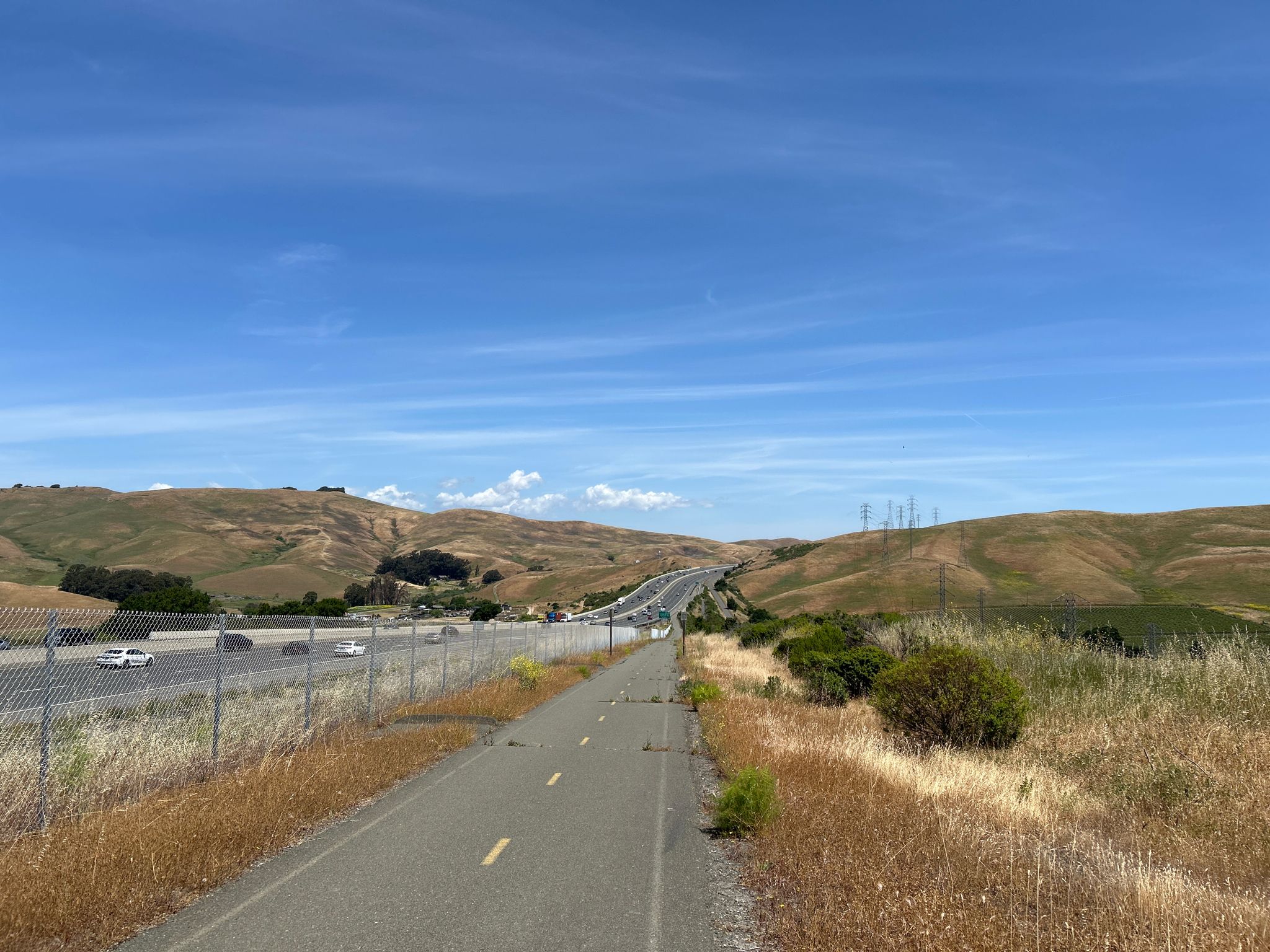 Paved path running parallel to a highway, with dry rolling hills. - Lake Herman Park – Benicia State Recreation Area loop from Green Valley Office Park