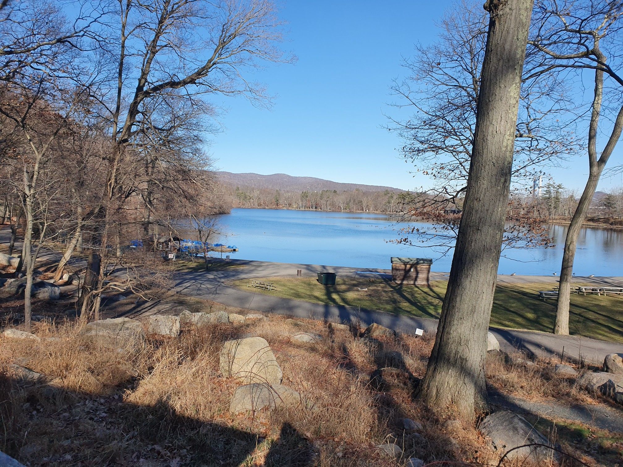 Calm lake with a boat launch, surrounded by bare trees under a bright blue sky. - Perkins Memorial Tower – Hessian Lake loop from Fort Montgomery