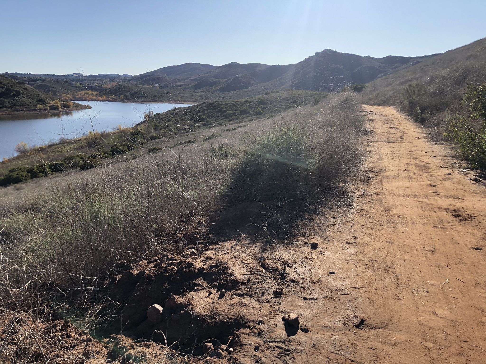 A dirt path runs alongside a lake with distant hills under bright sun. - Bernardo Mountain Loop via Coast to Crest Trail