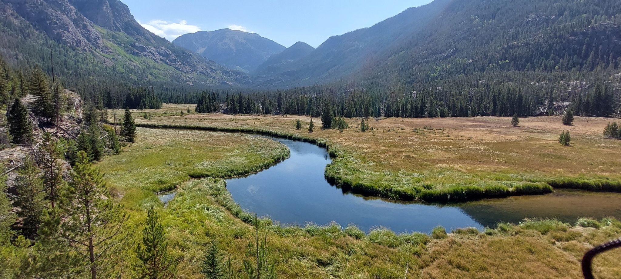 River winding through a grassy valley with mountains and forests under clear sky. - Lake Verna via East Inlet Trail