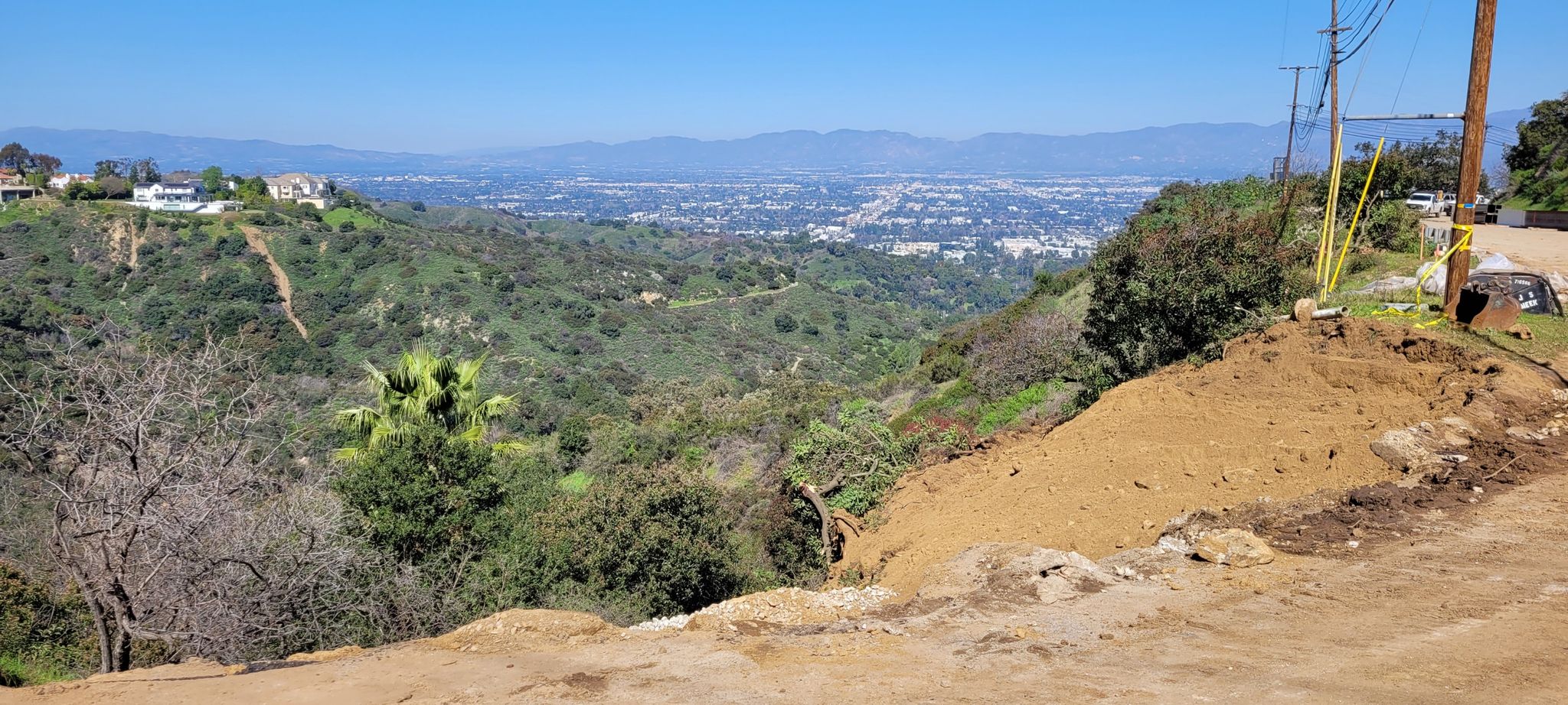 Panoramic view of green hills, distant city, and mountains under clear sky. - Mulholland Drive Loop
