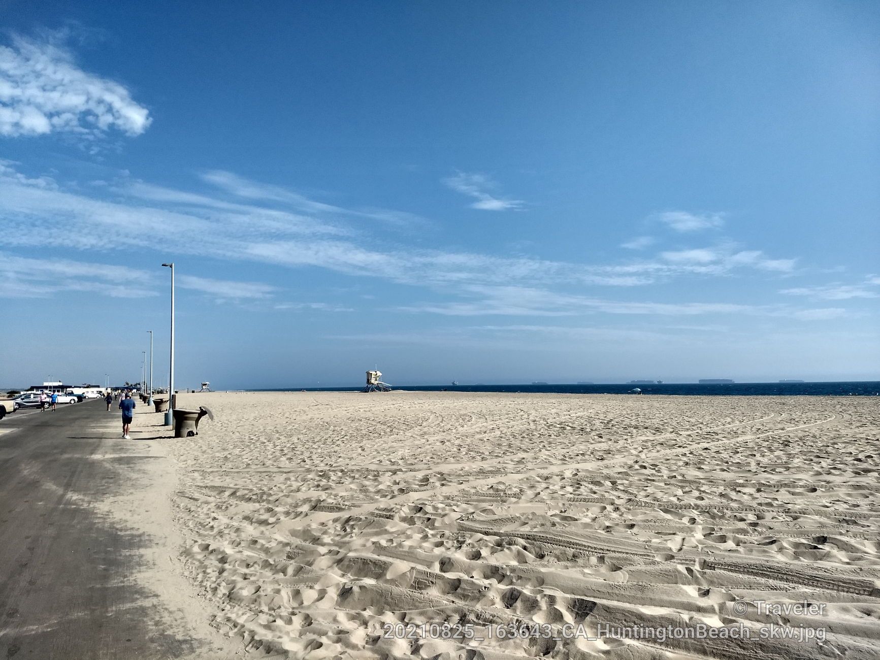 Wide sandy beach next to a paved path, with ocean and a few people. - Huntington Beach Bike Trail