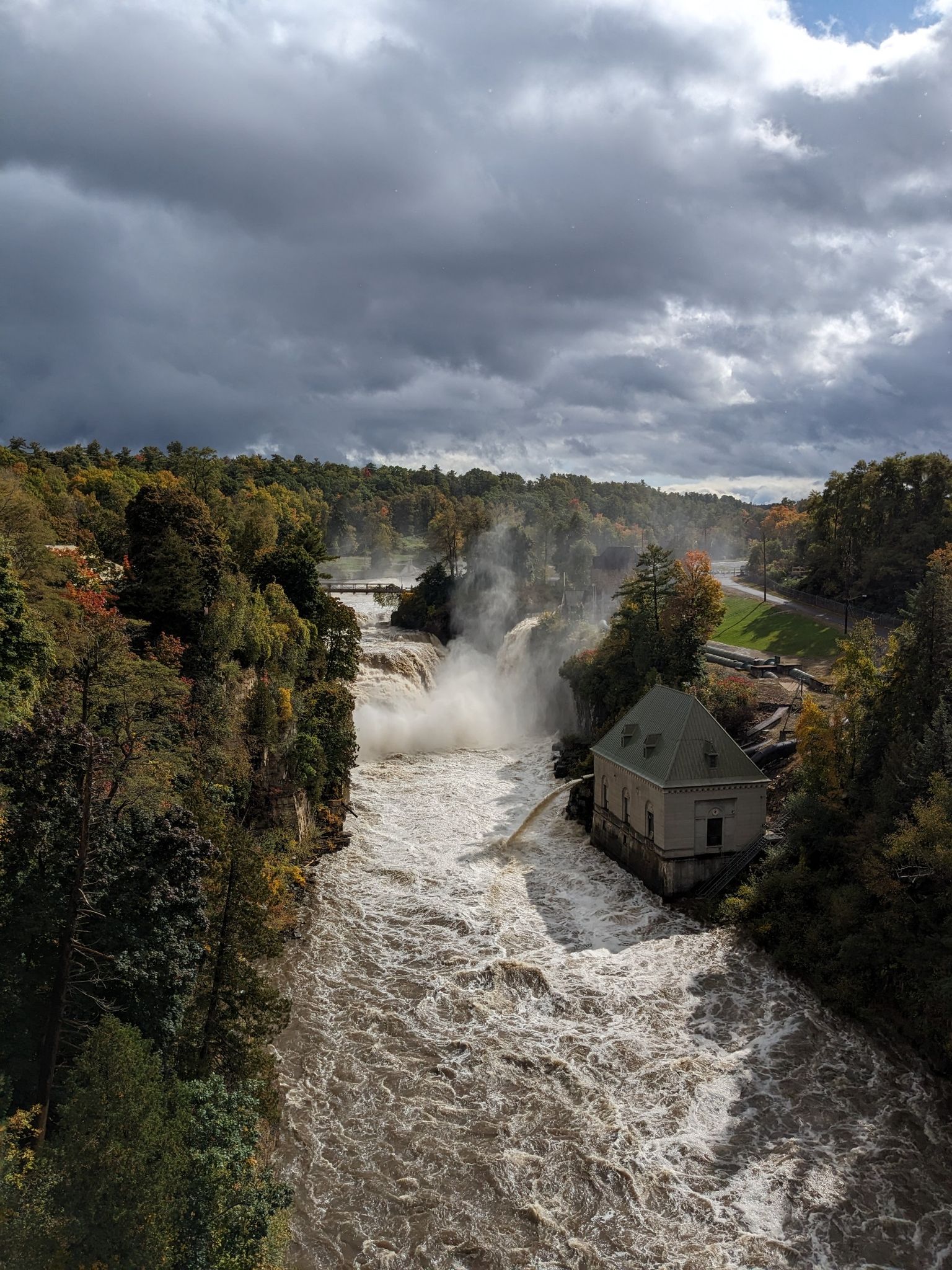 Rushing river with waterfall and building under a cloudy sky. - Ausable Chasm – Ausable Chasm loop from Ausable Acres Tennis Courts