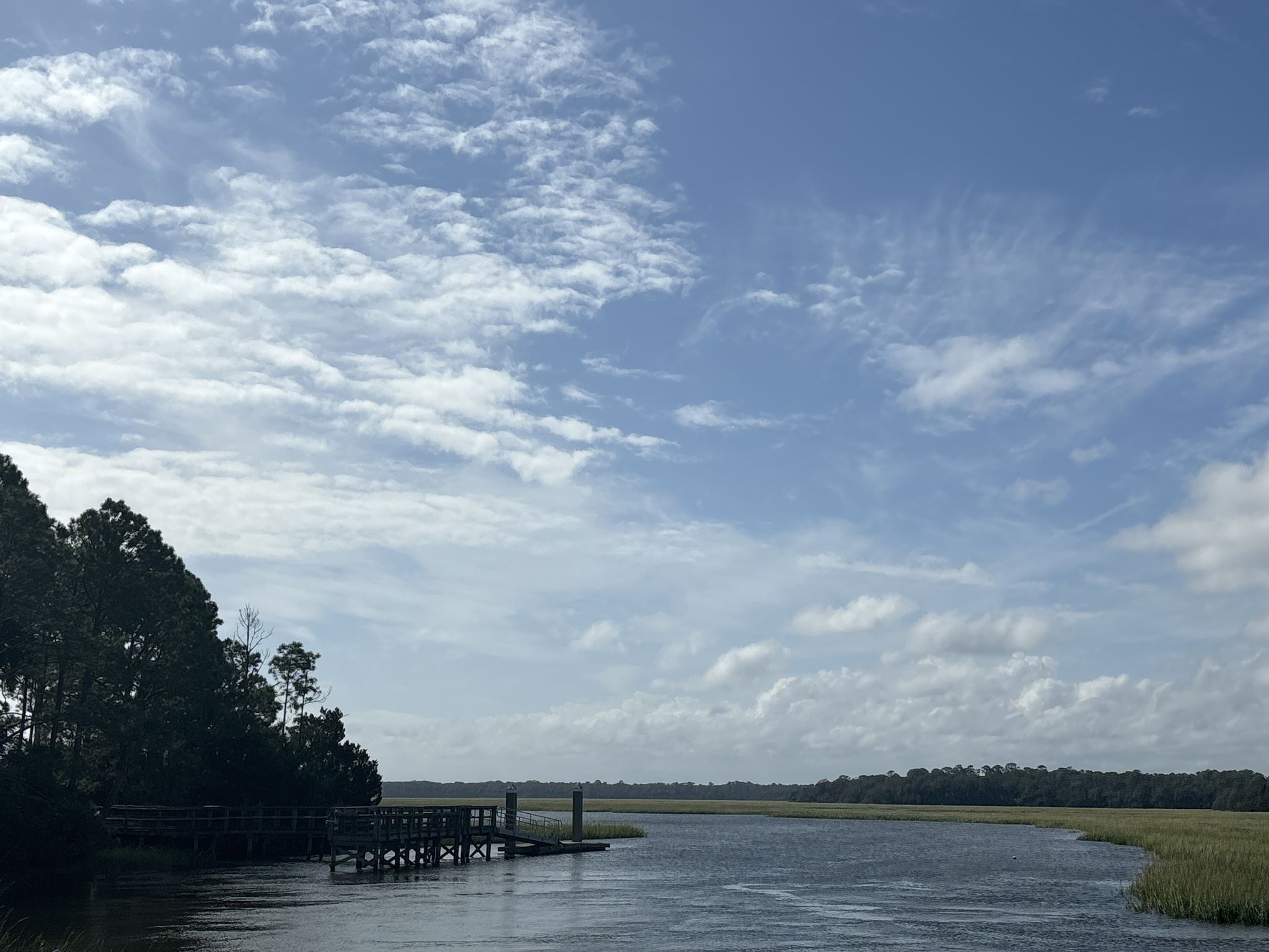 River with a wooden dock, marshland, and trees under a cloudy blue sky. - East Coast Greenway: Amelia Island