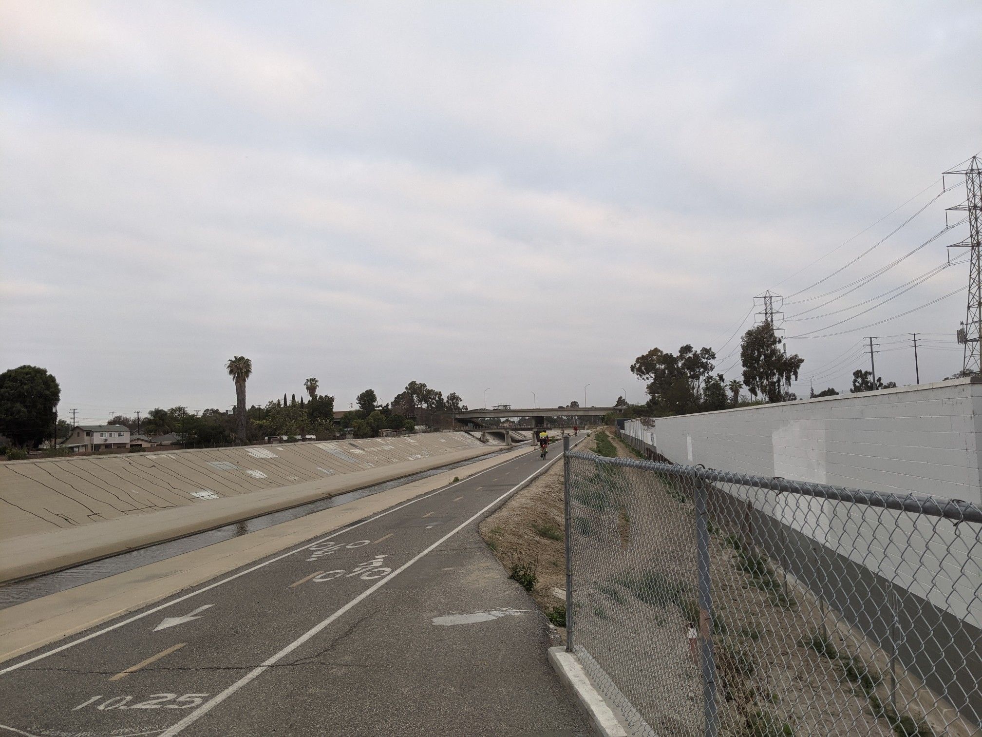Overcast view of a wide concrete channel with a paved path. - San Gabriel River Trail: Caruthers Park to Liberty Park