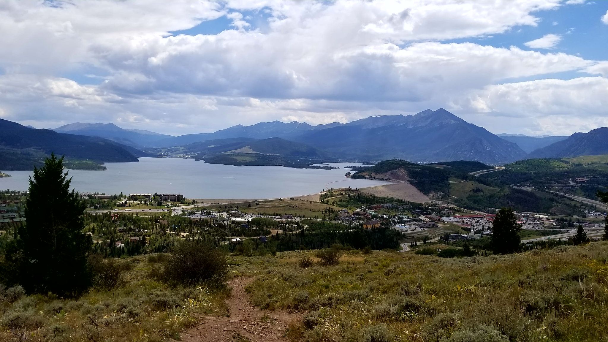 Overlook of a large lake, town, and mountains under a cloudy sky. - Ptarmigan Peak Trail