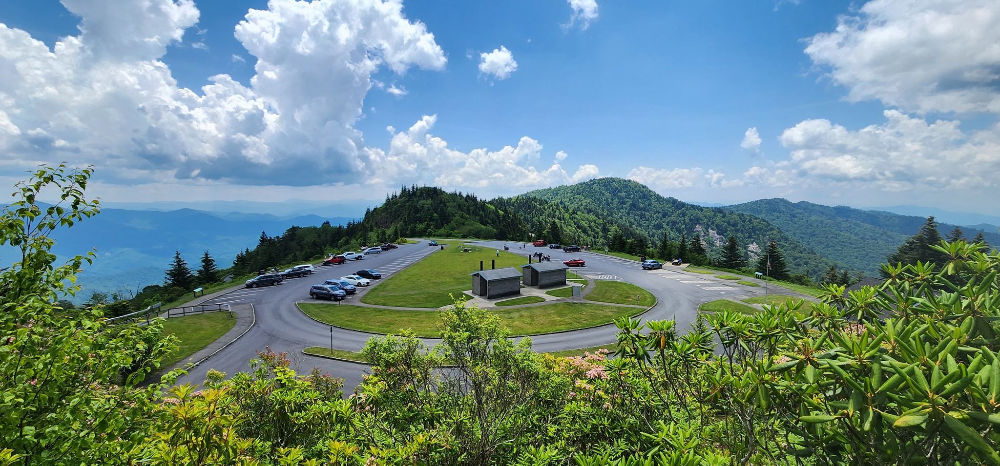 Panoramic view of a mountain parking lot, small buildings, and distant green peaks under a cloudy sky. - Waterrock Knob Trail
