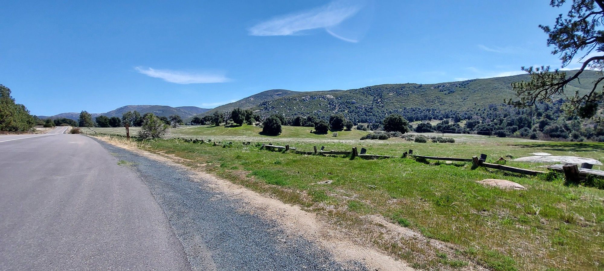 Paved road next to a green grassy field with scattered trees and hills. - Trail near State Highway 79 – Cold Spring Trail loop from Oakzanita Peak