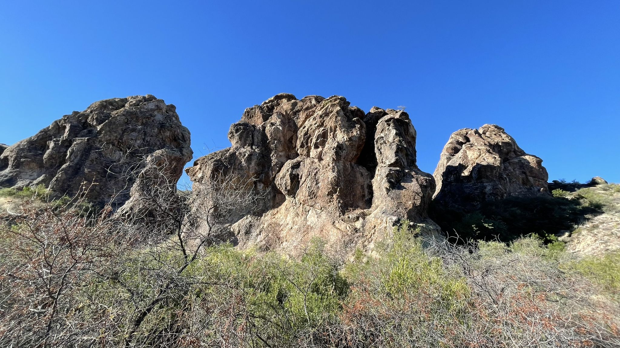 Large rock formations under a clear blue sky, with sparse desert plants. - Dutchman, Boulder Canyon, and Second Water Trail Loop