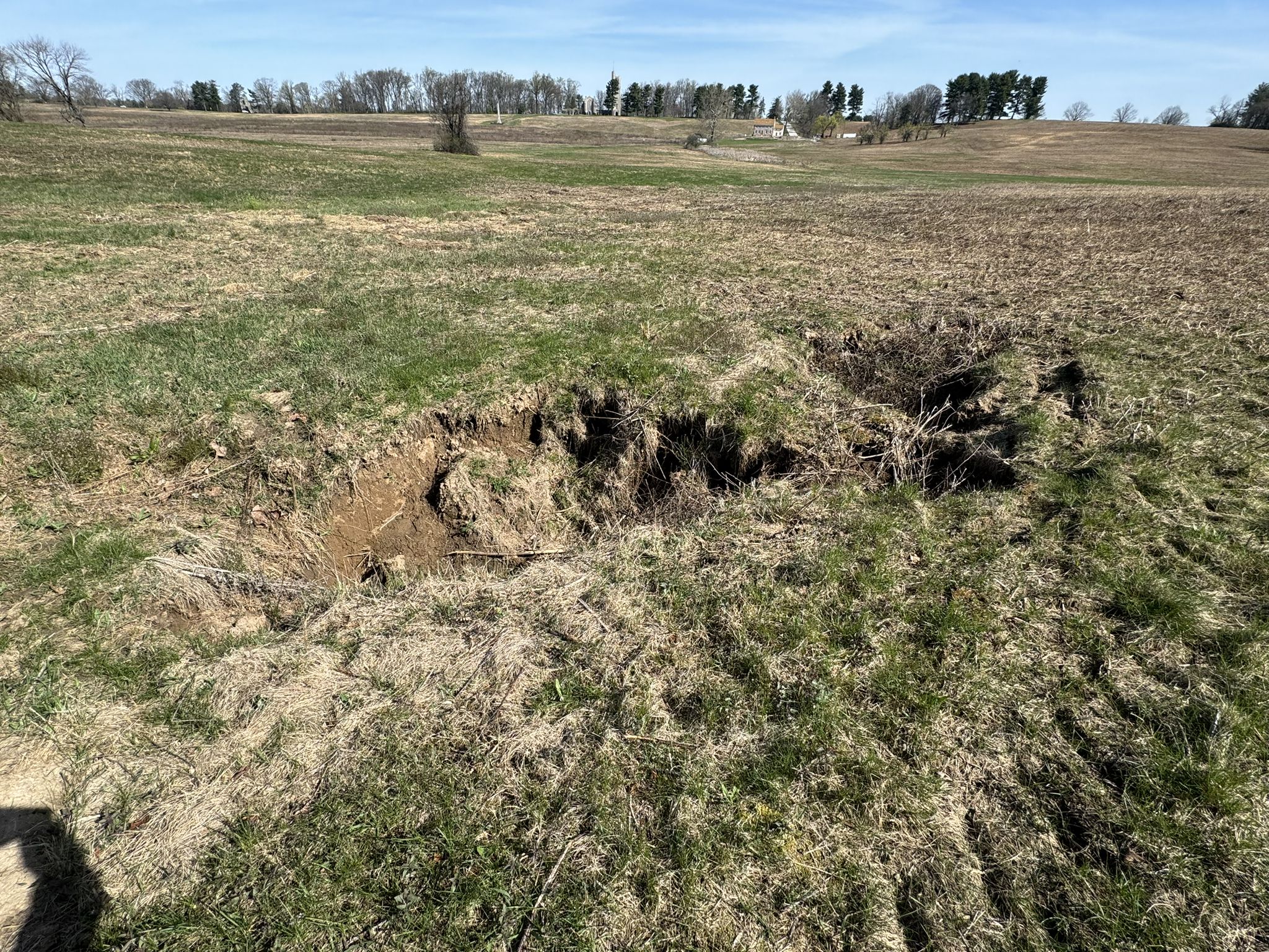Large hole in a dry, grassy field under a clear blue sky. - Chapel and Joseph Plumb Martin Trail Loop