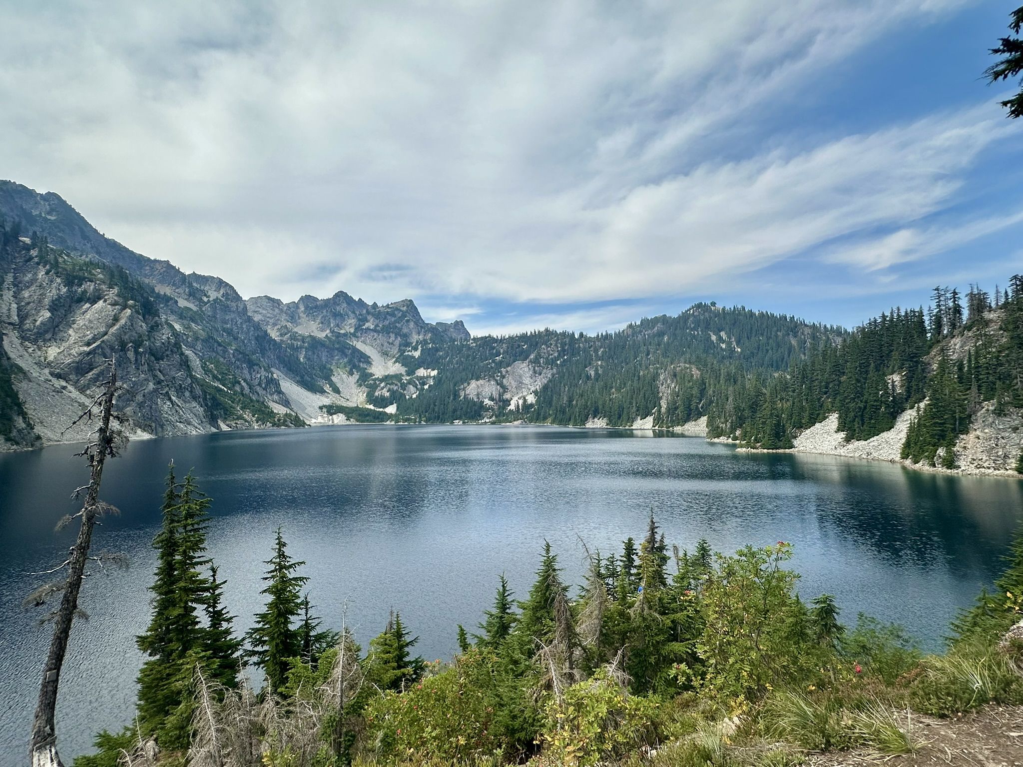 Calm mountain lake surrounded by rocky peaks and evergreen forests under cloudy sky. - Snow Lake Trail
