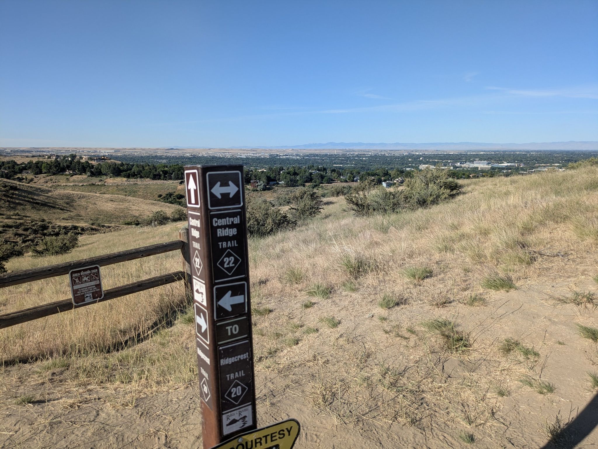 Trail marker post on a dry, grassy hillside overlooking a distant city. - Three Bears and Two Point Trails Loop