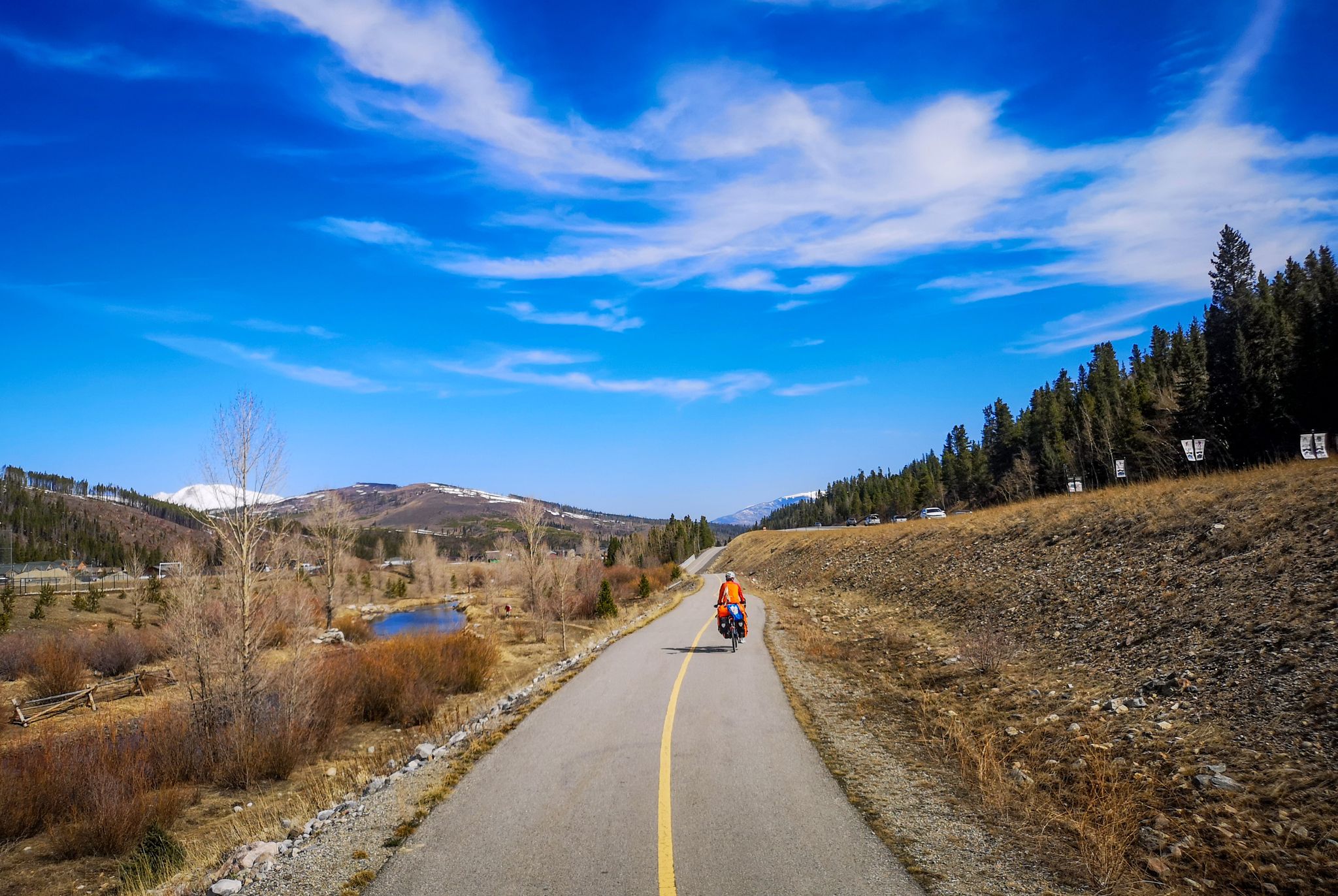 Person cycling on a paved path through a sunny mountain landscape. - Upper Blue Recpath