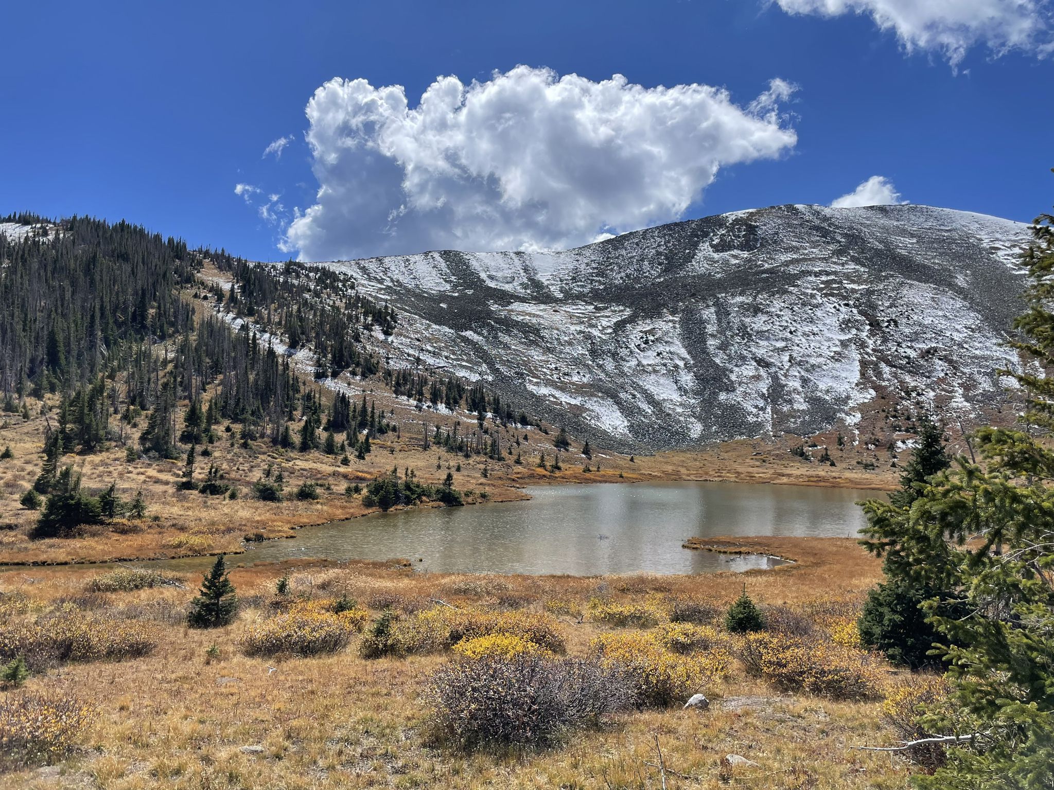 A serene lake reflects a snow-capped mountain under a bright blue sky. - Treasure Mountain and Beaver Creek Loop