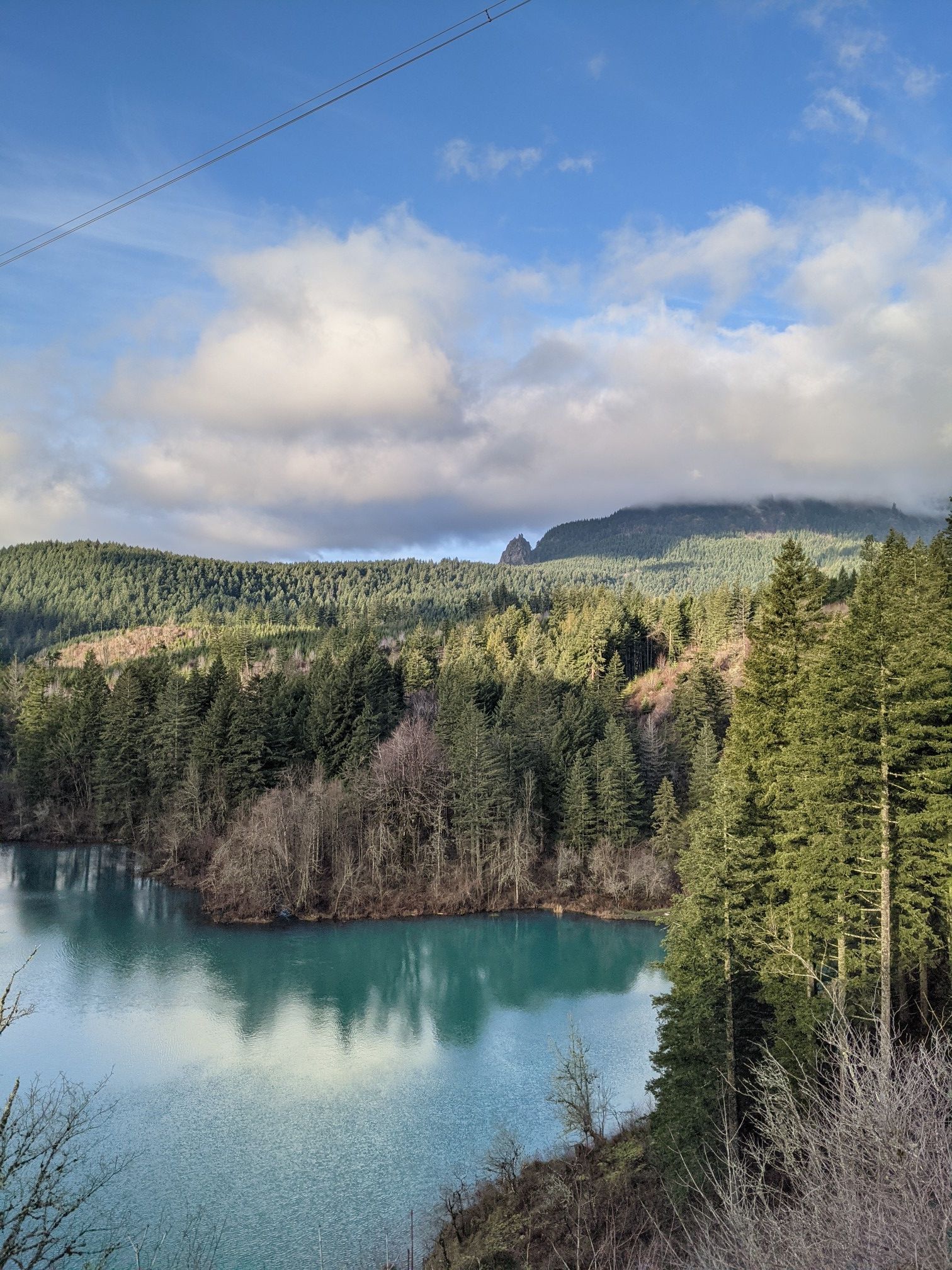Turquoise lake surrounded by dense forest and mountains under a partly cloudy sky. - Gillette Lake via Pacific Crest Trail