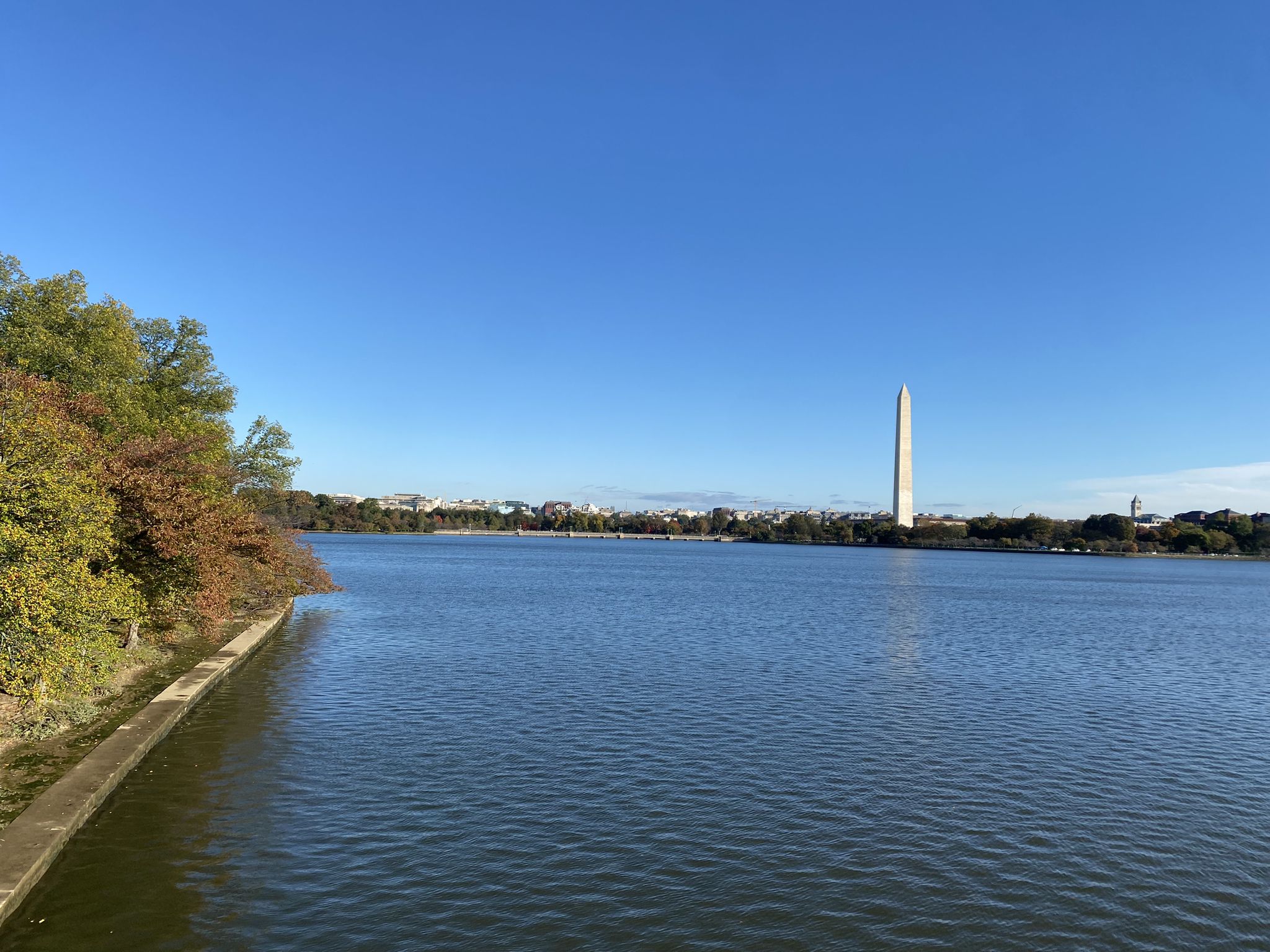 A calm lake with autumn trees on the left and a distant tall monument. - Memorial Trail via Jefferson Memorial