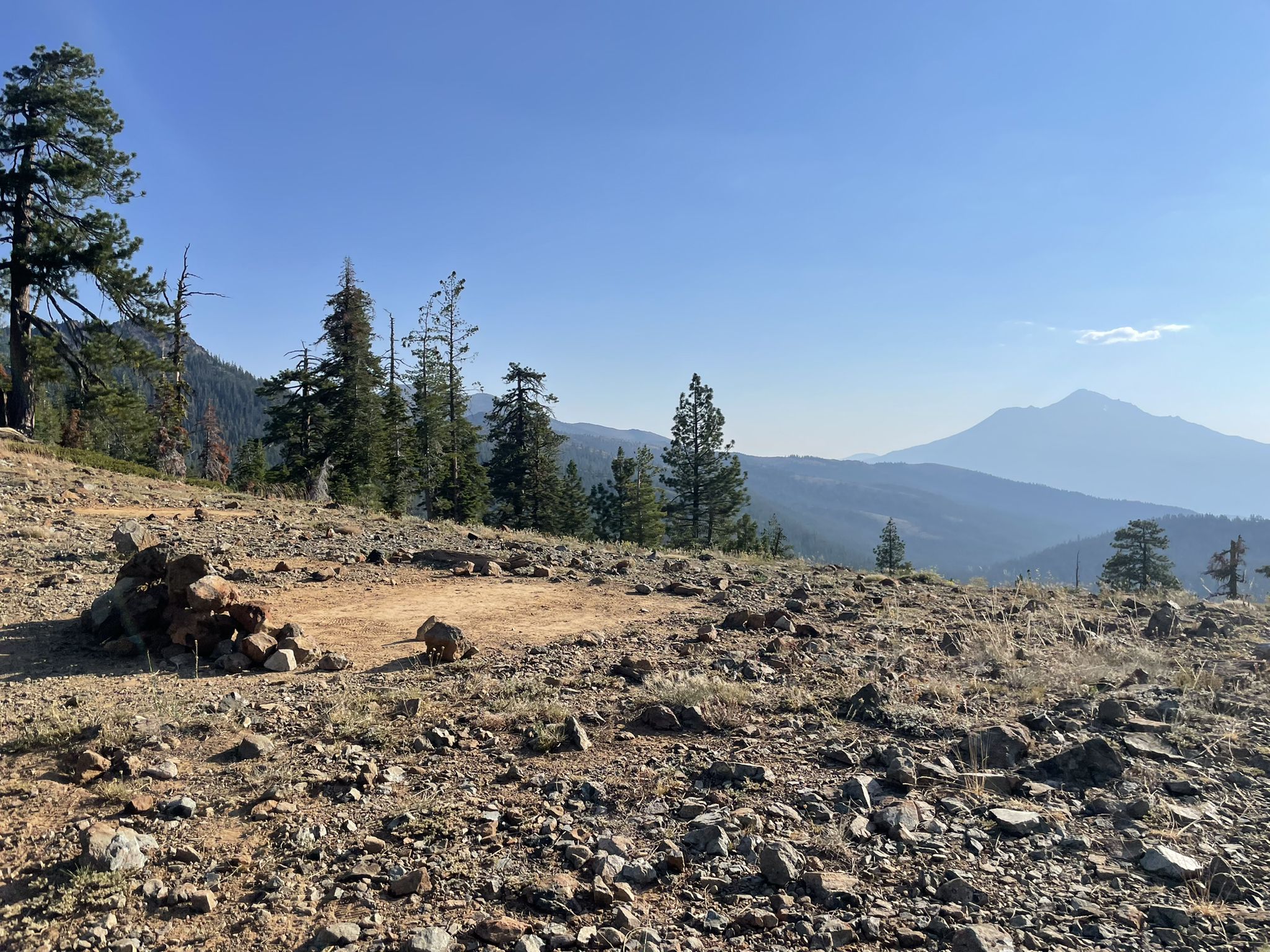 A rocky, open hillside with scattered trees and hazy mountains under a clear sky. - Porcupine Lake via Pacific Crest Trail