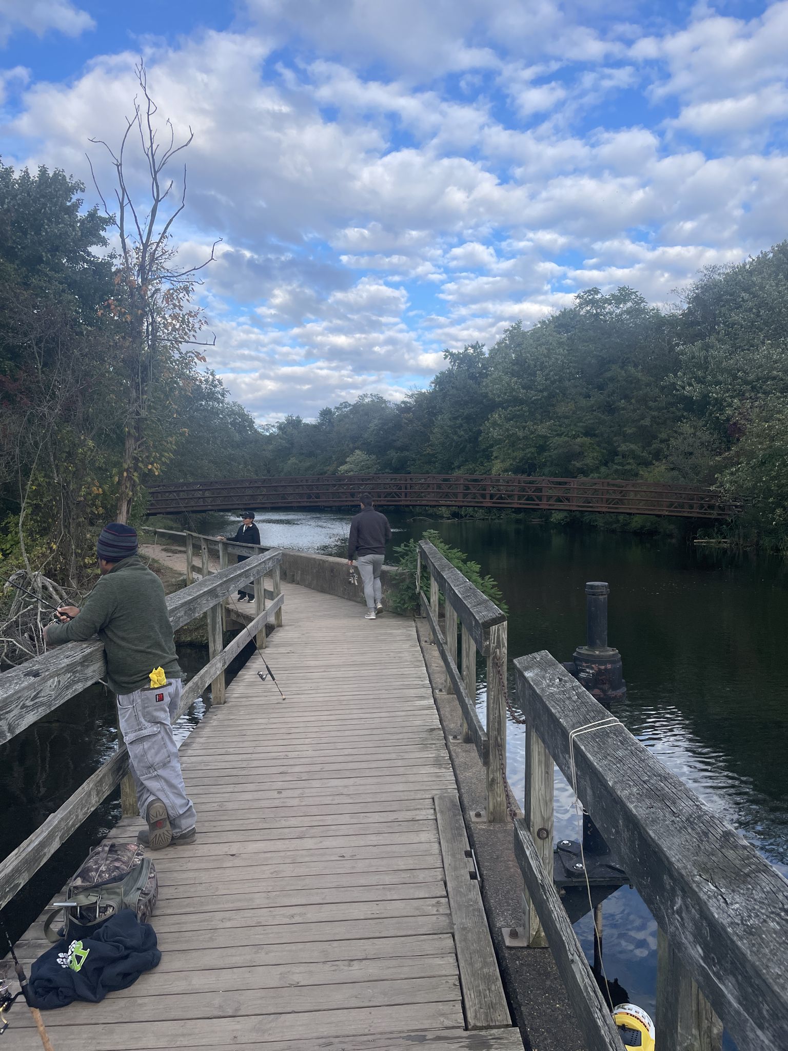 People fishing from a wooden boardwalk next to a river under a cloudy sky. - Cranbury loop from Rocky Hill