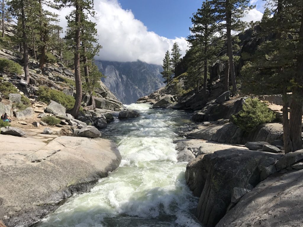 Rushing river through a rocky gorge with pine trees under a cloudy sky. - Upper Yosemite Fall Trail