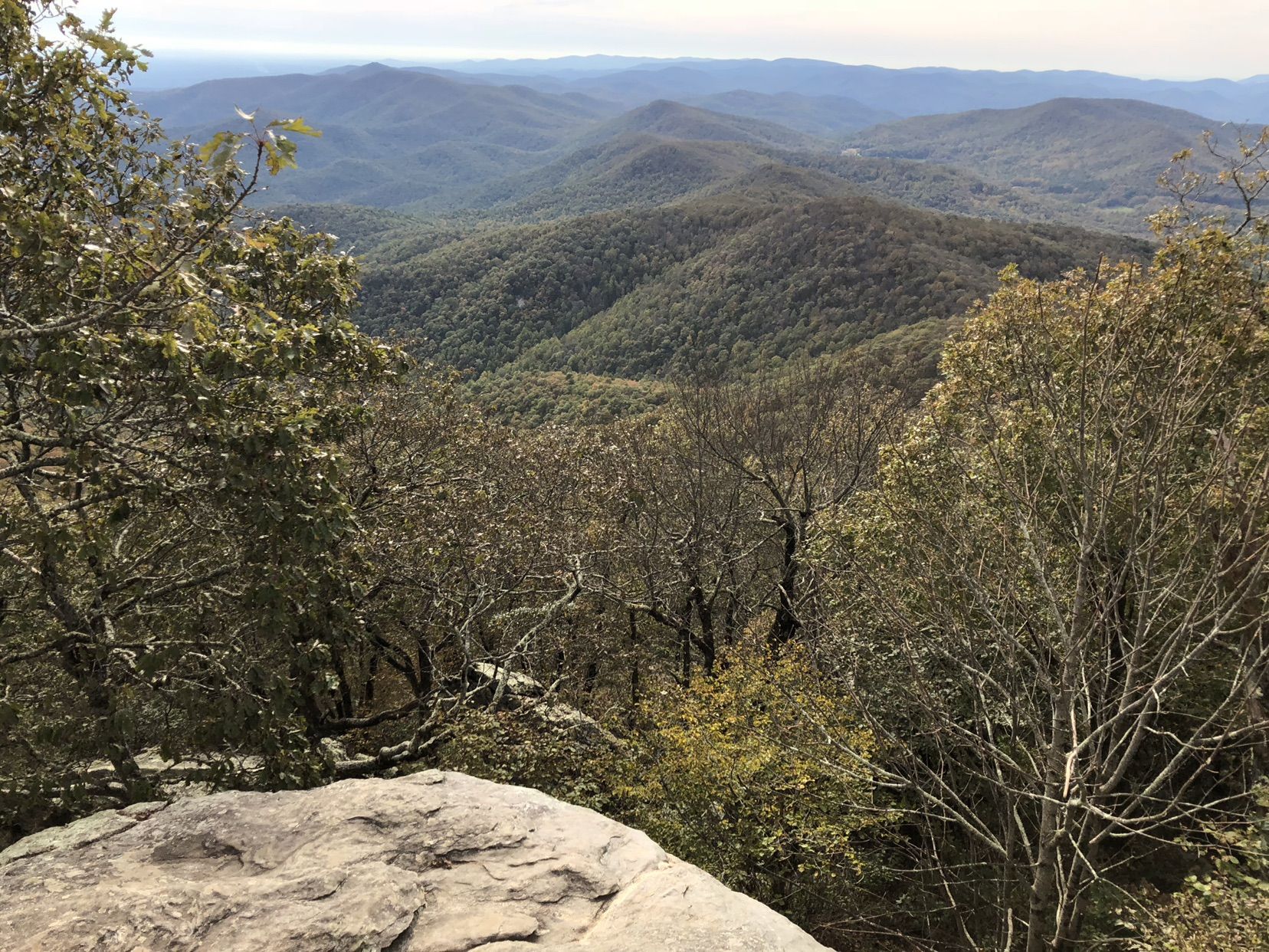 Overlook of forested mountains under a hazy sky, with rocks and trees. - Duncan Ridge Trail to Blood Mountain
