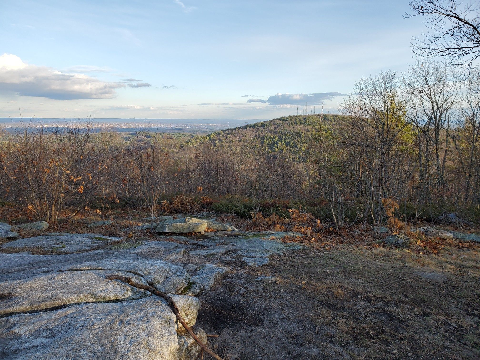 Rocky overlook with bare trees and distant green hills under a bright sky. - North Uncanoonuc Mountain via White Dot and Red Dot Trail