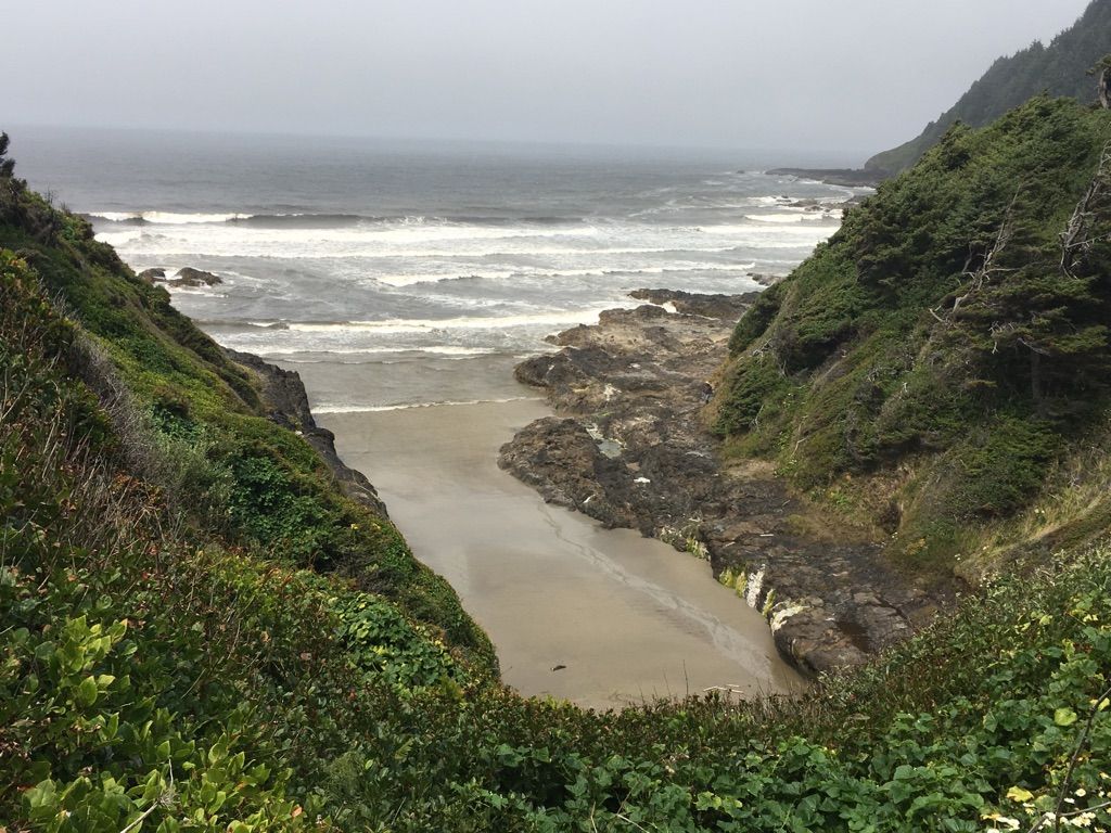 A sandy beach in a rocky cove under an overcast sky. - Cape Perpetua Visitor Center – Good Fortune Cove loop from Cape Perpetua Special Interest Area