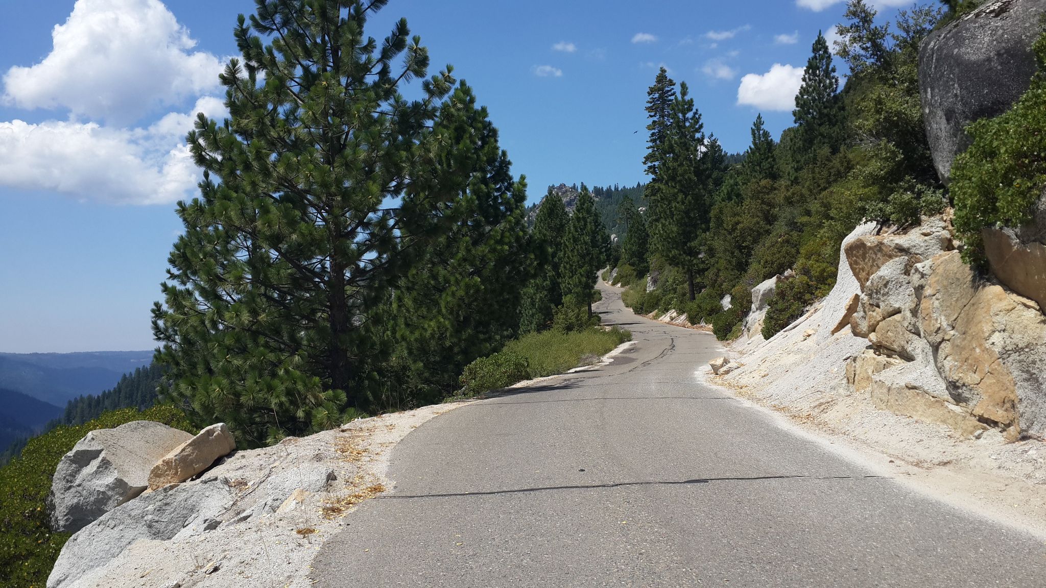 A winding mountain road with pine trees and rocky slopes under a sunny sky. - Wrights Lake loop