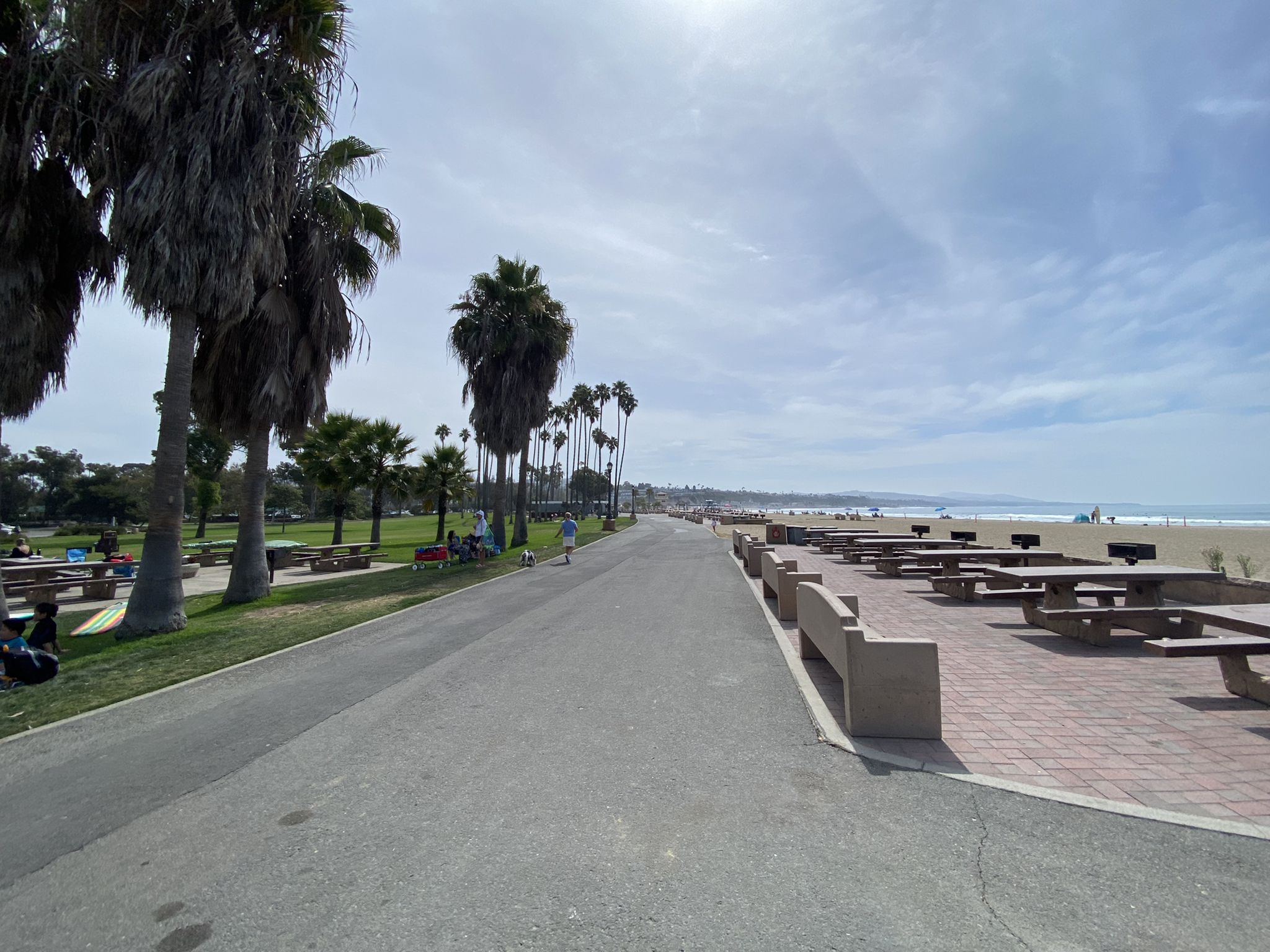 Paved path lined with palm trees and picnic tables next to a sunny beach. - Mission San Juan Capistrano – Descanso Park loop from Trabuco Canyon