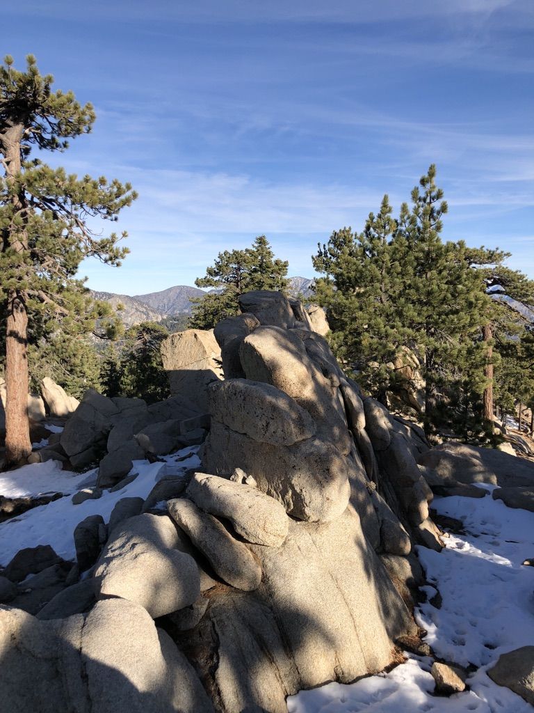Sunny mountain landscape with large rocks, pine trees, and patches of snow. - Waterman Mountain Loop Trail