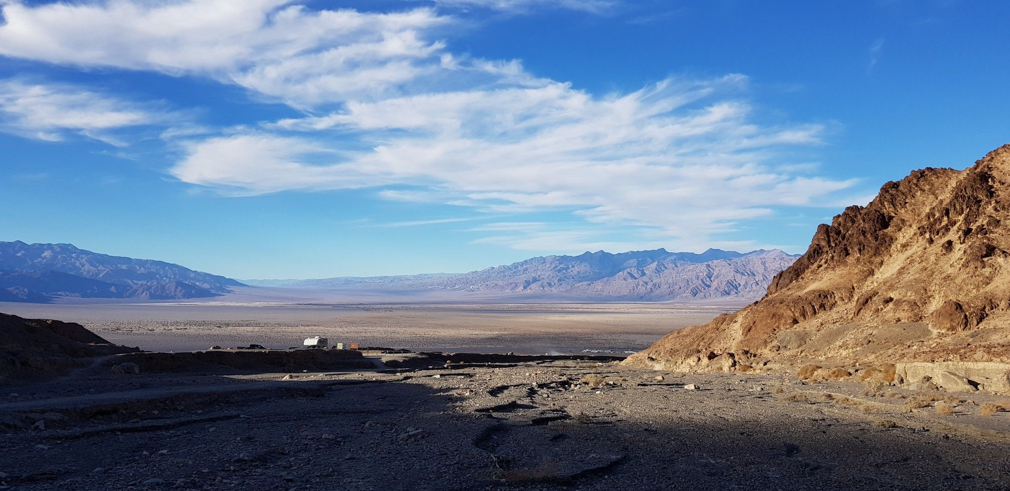 Vast desert valley with distant mountains under a partly cloudy blue sky. - Mosaic Canyon Trail