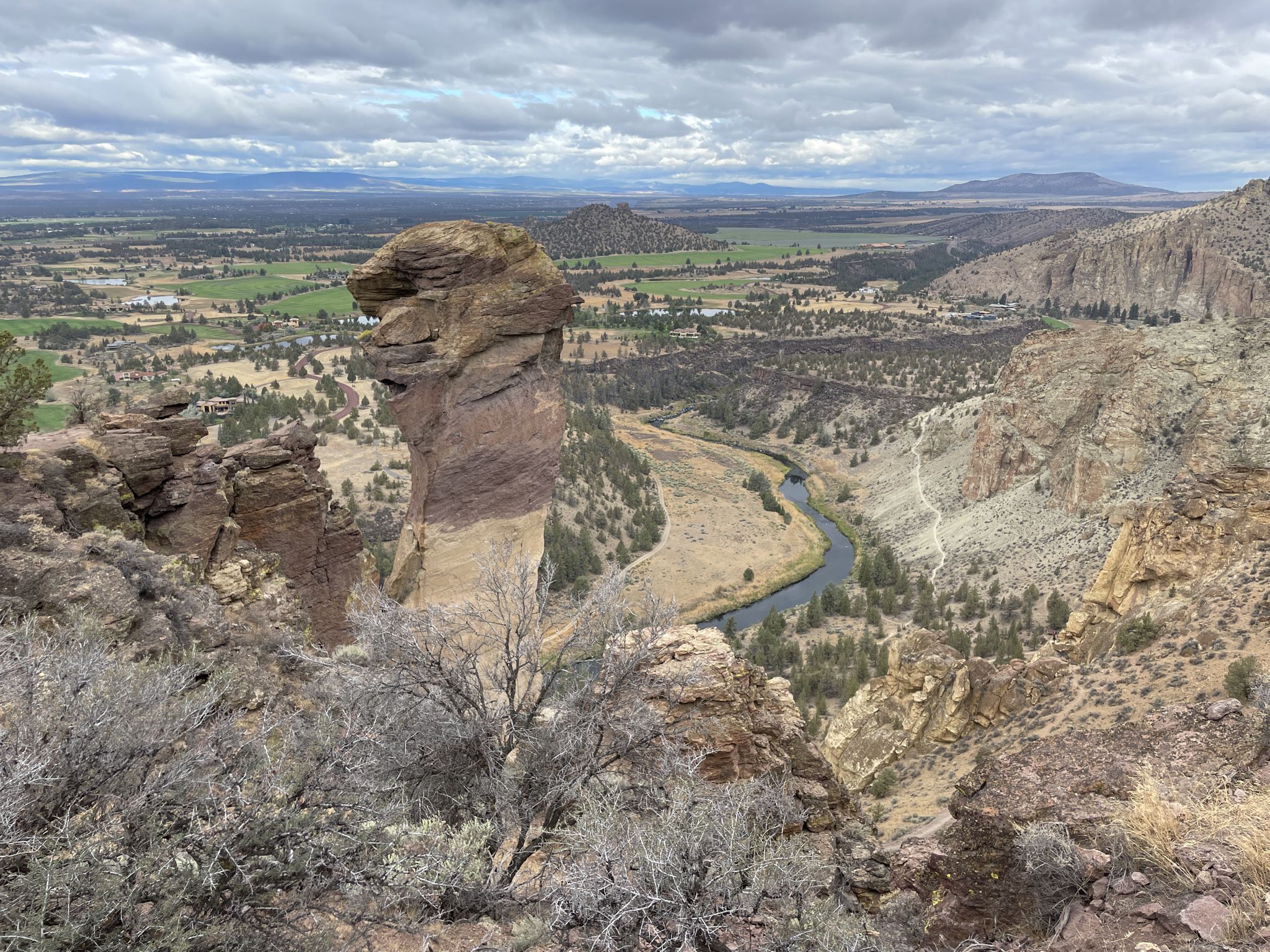 A distinctive rock formation stands above a winding river in a vast valley. - Misery Ridge Trail