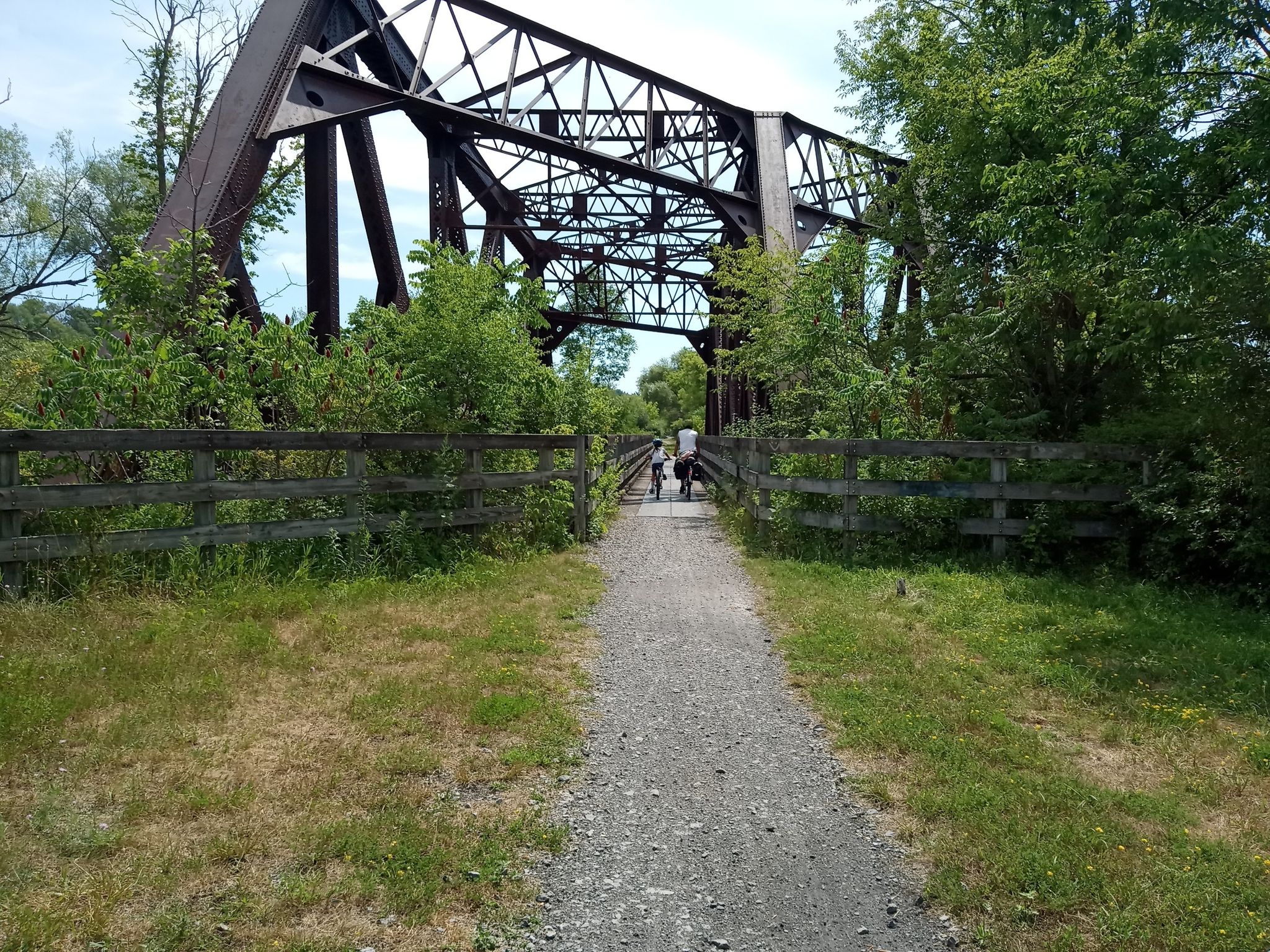 Gravel path leading to a large metal truss bridge with two distant cyclists. - Junction Hill – Wadsworth Junction loop from Village of Scottsville