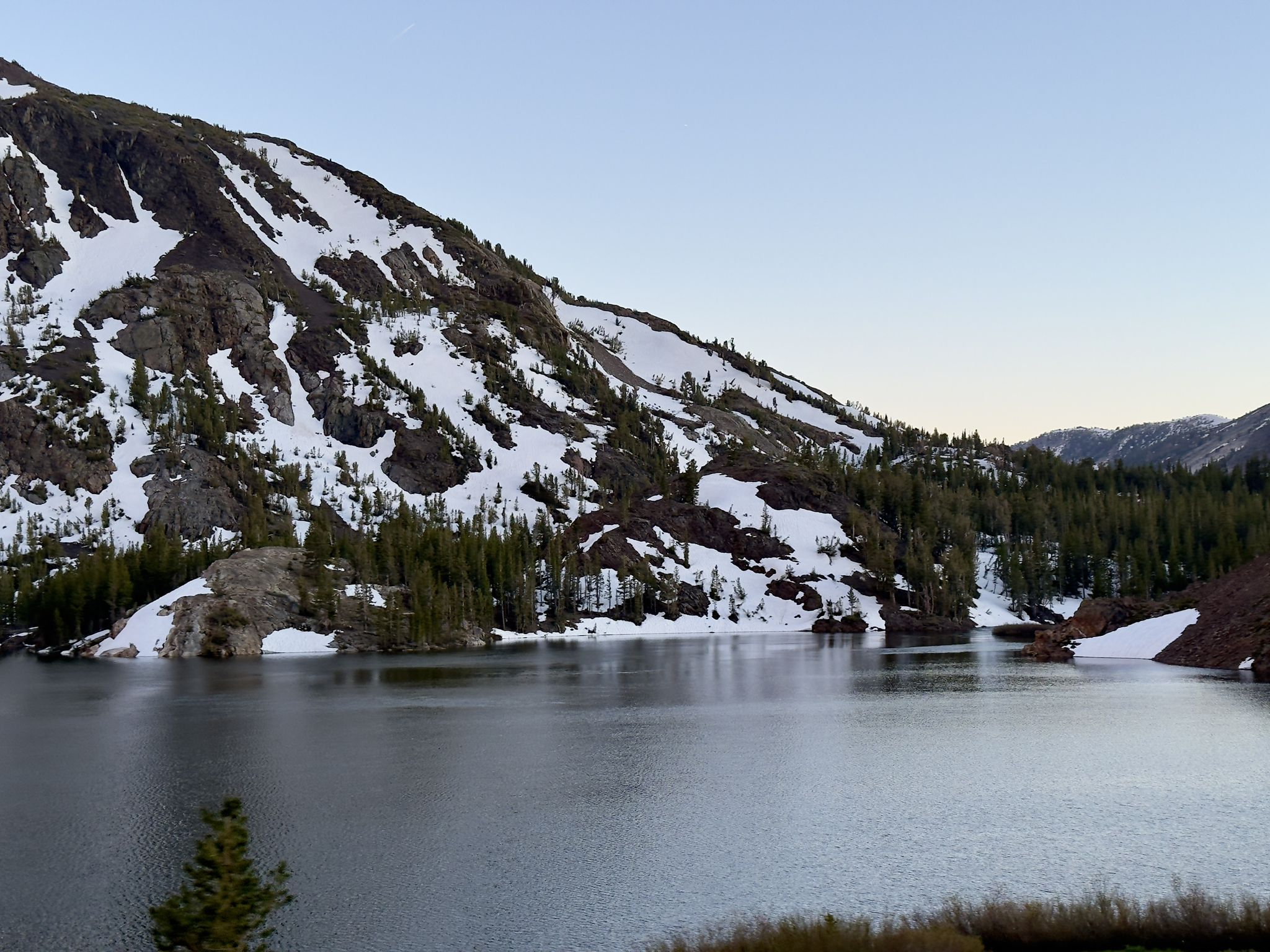 Serene lake surrounded by snow-dusted mountains and evergreen trees. - Tioga Lake North overlook – Tioga Pass loop from Lee Vining