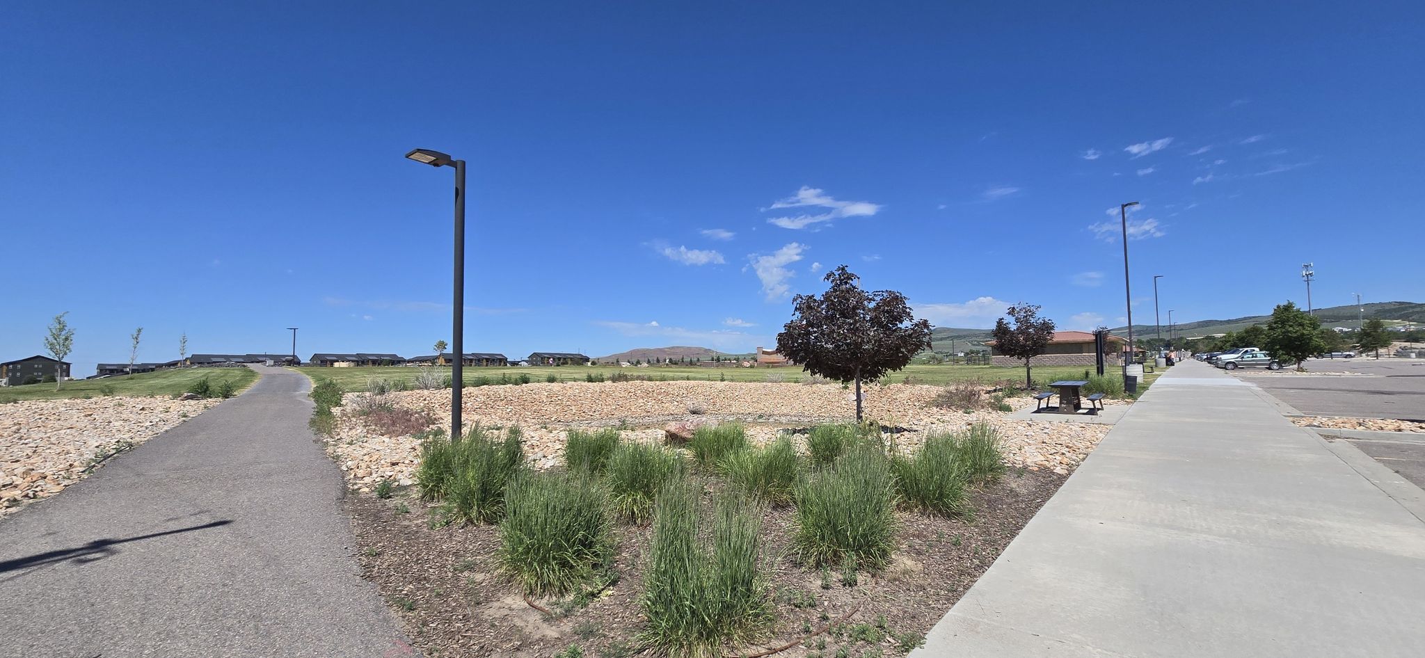 Two paved paths converge in a sunny, open landscape with distant buildings. - Portneuf Wellness Complex Loop