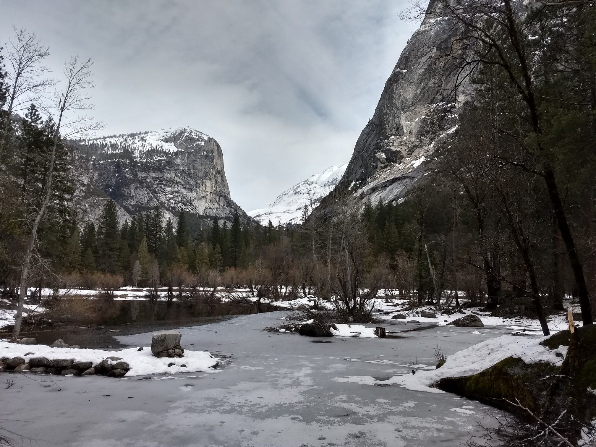 Icy river and snow-covered banks in a valley between large, rocky mountains. - Yosemite Village to Mirror Lake